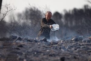 hombre arrojando agua de bidón de plástico sobre una zona quemada