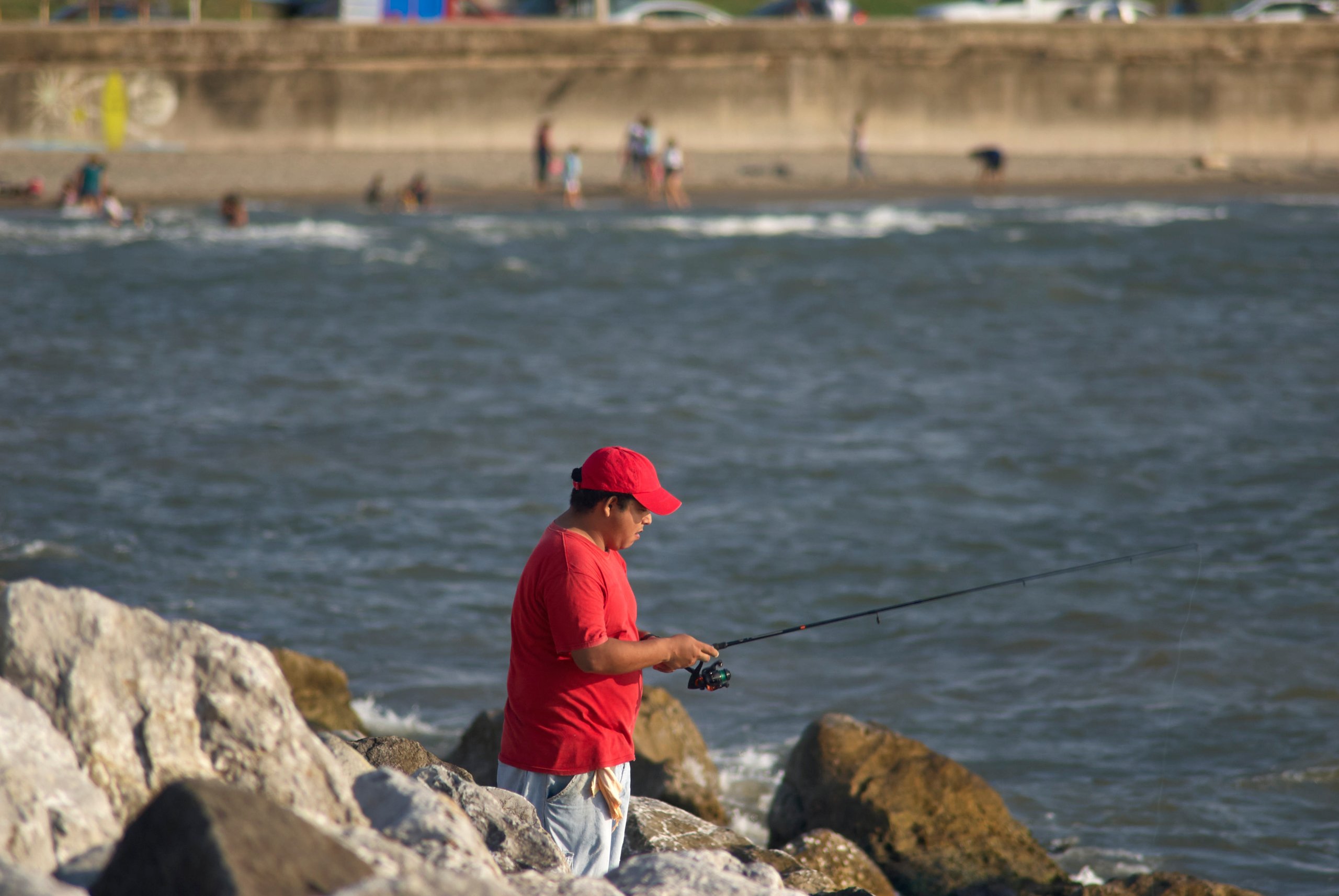 Un hombre, con una camisa roja y una gorra roja, pescando con una caña