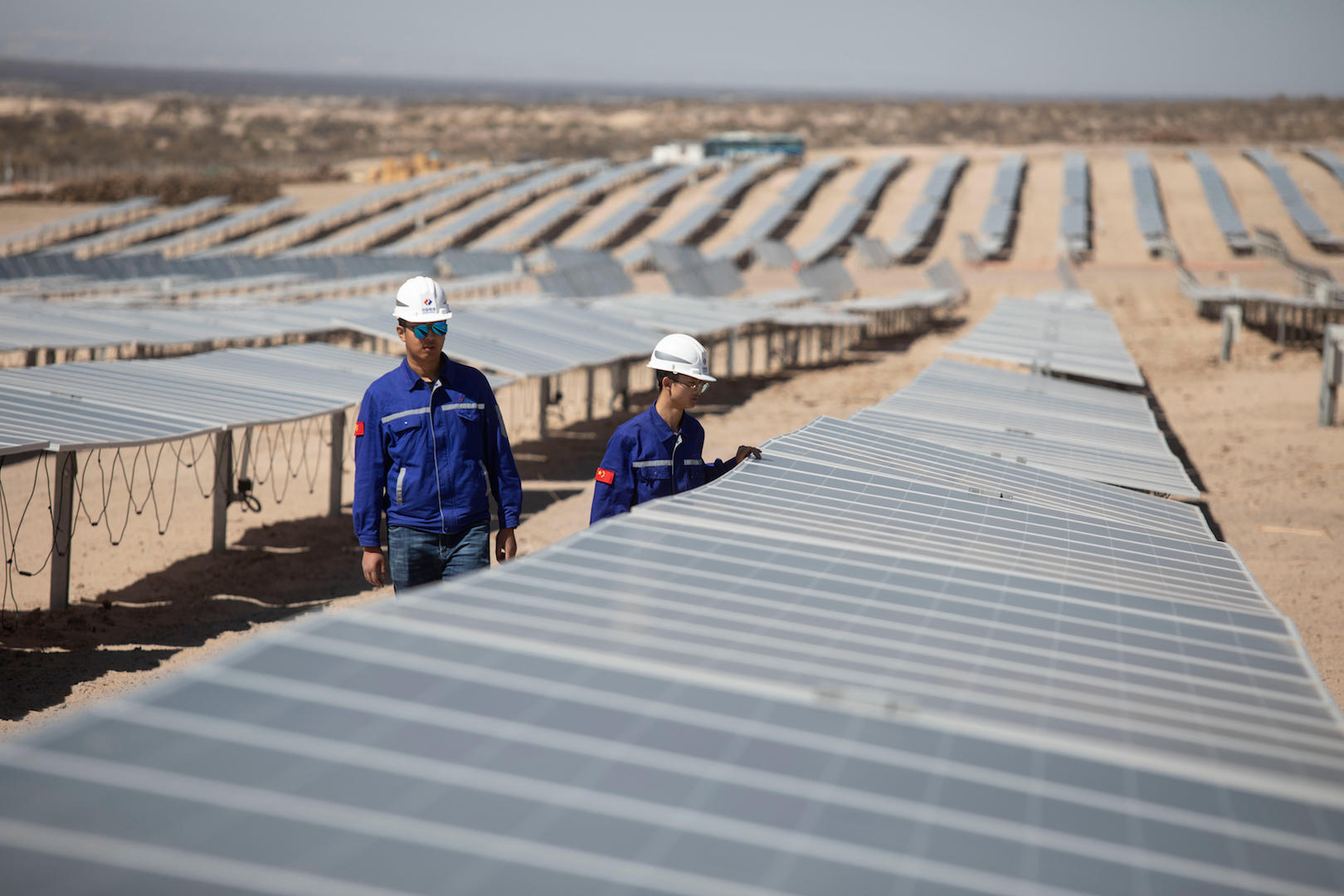 Dos ingenieros, vestidos de azul y con cascos blancos, inspeccionan paneles solares