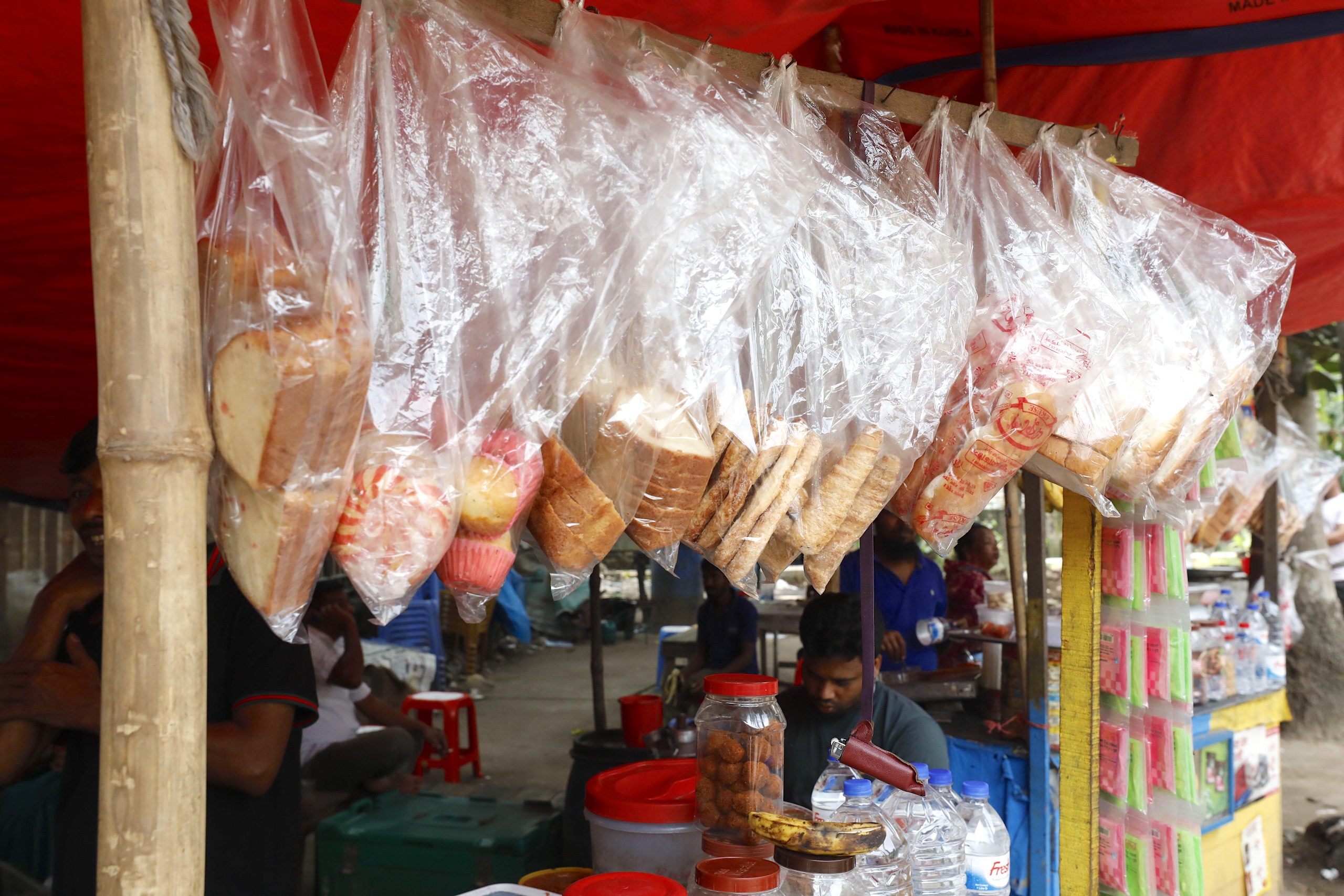 Plastic bags of sliced bread and snacks hang from a vendor's stand at an outdoor market