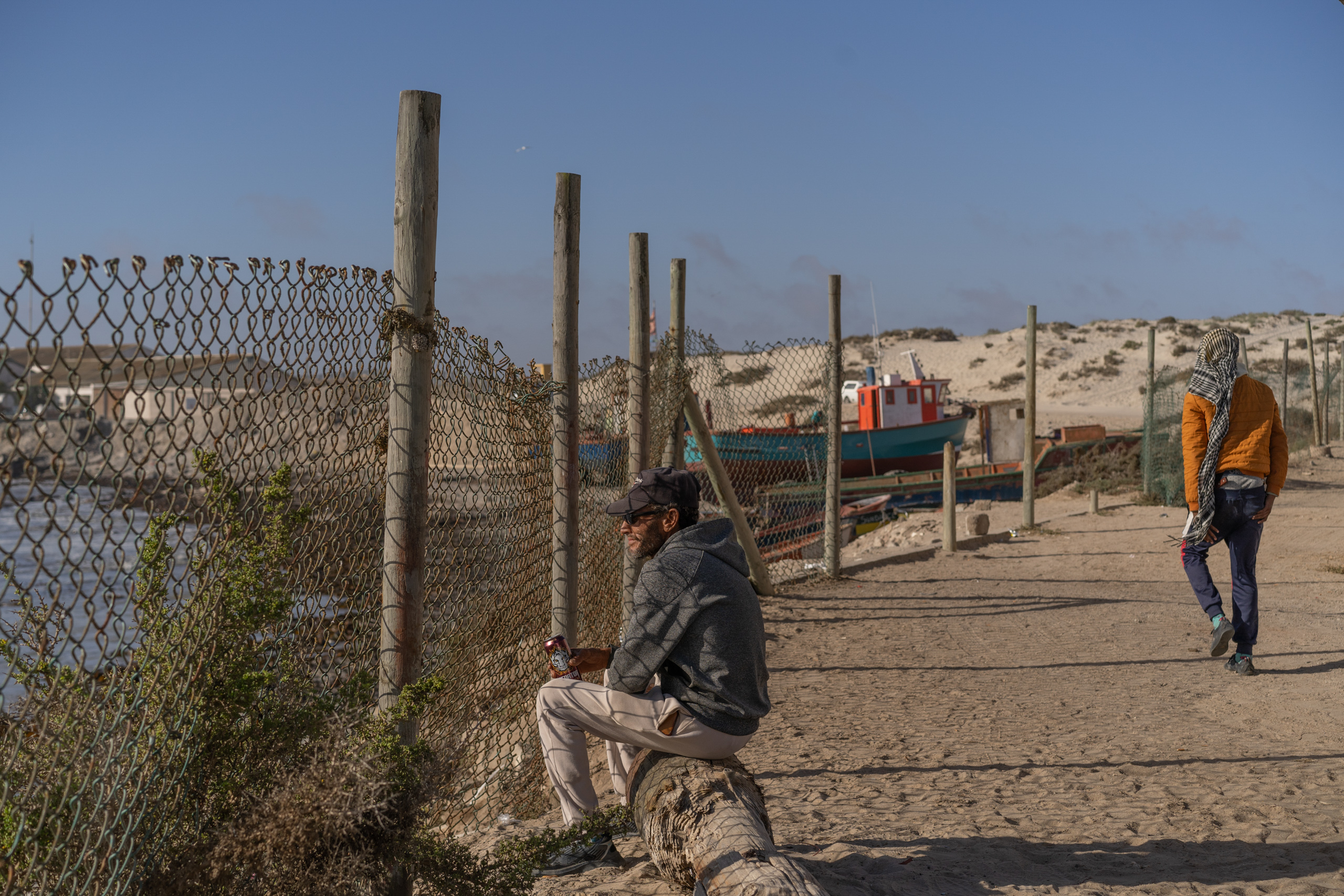 man sitting near rusty chainlink fence