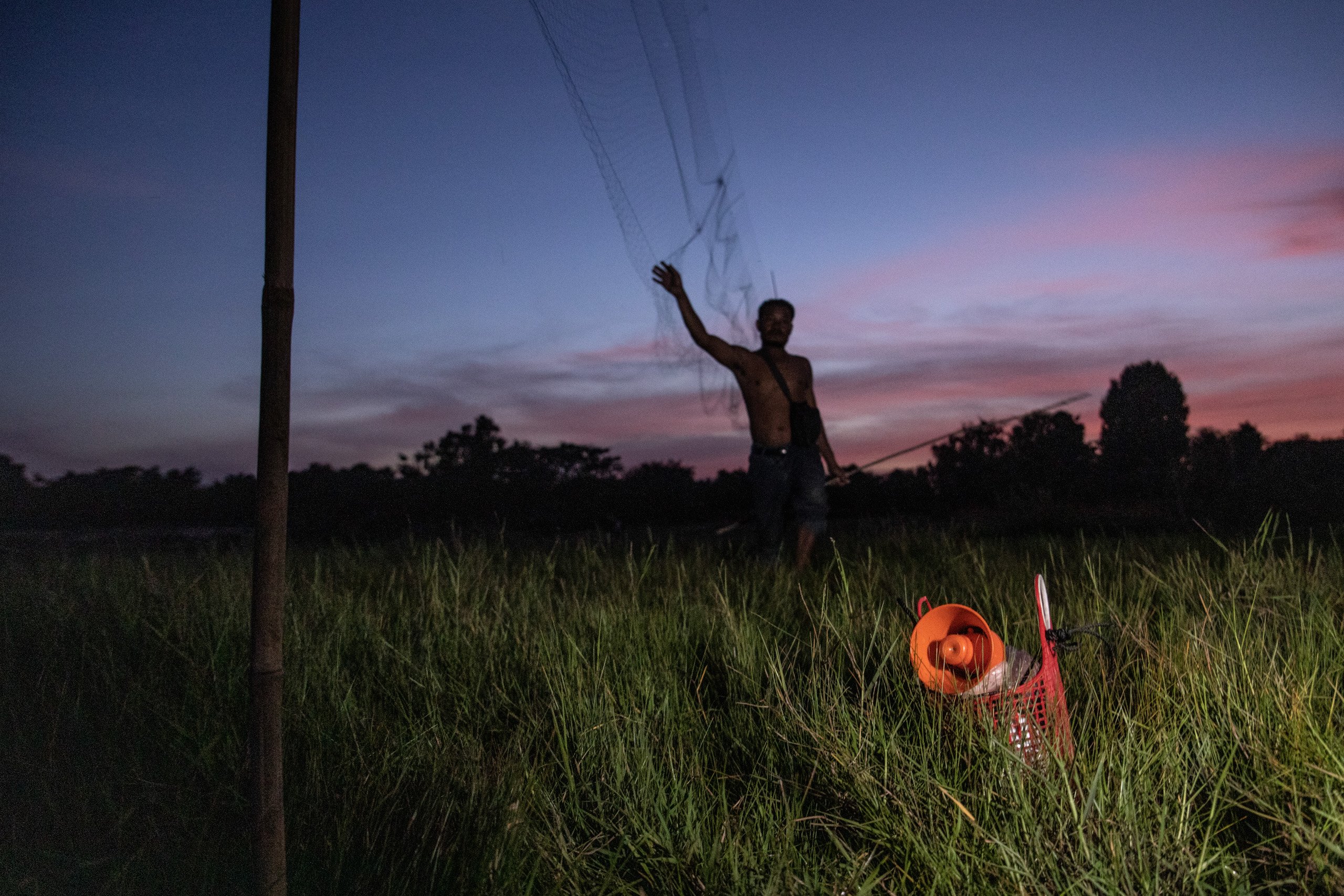 man throwing net out over long grass