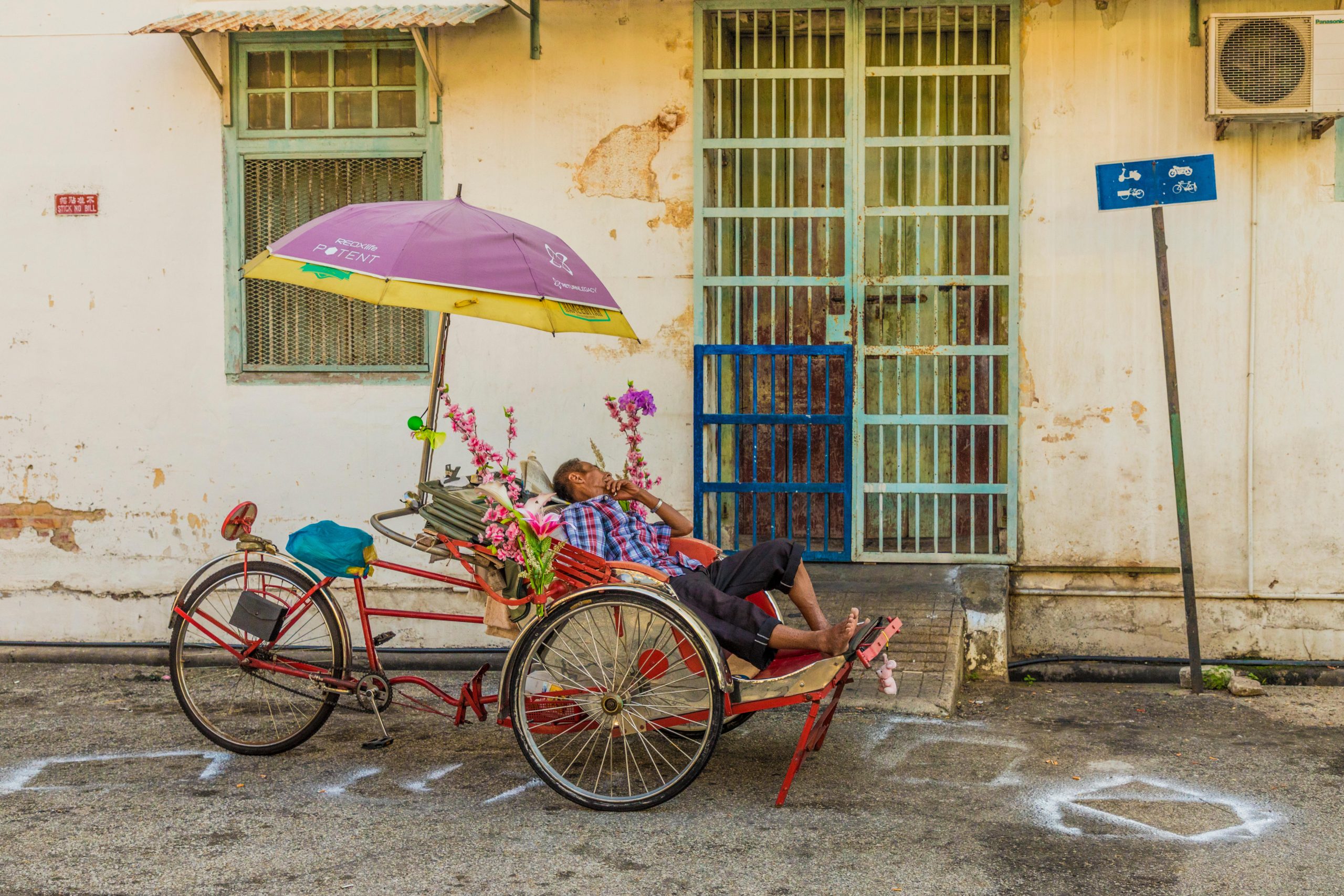 <p>A rickshaw cyclist rests under an umbrella during a hot day in Penang, Malaysia (Image: Chris Mouyiaris / Alamy)</p>