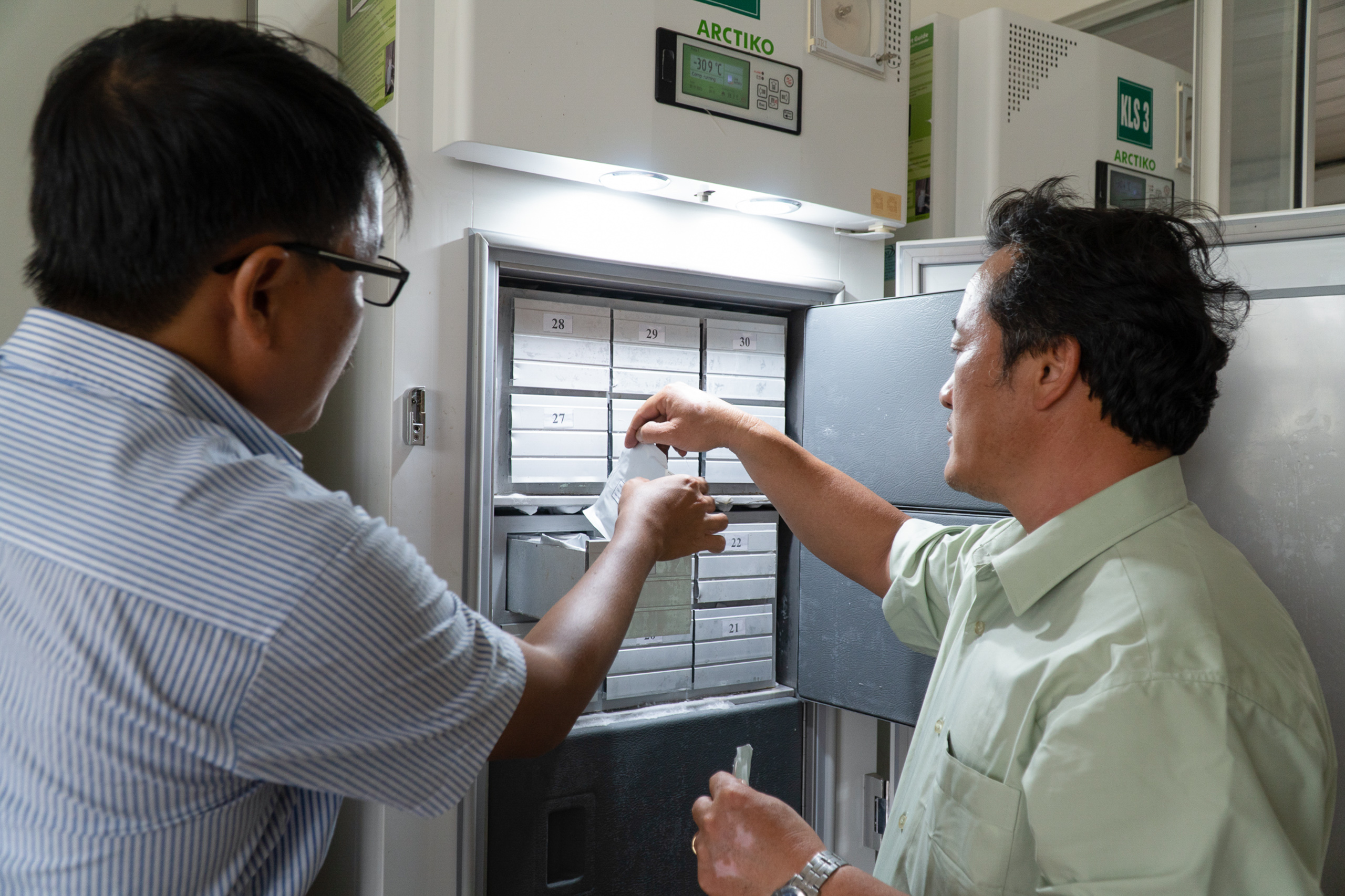 Two men standing side by side and putting seeds in the gene bank 