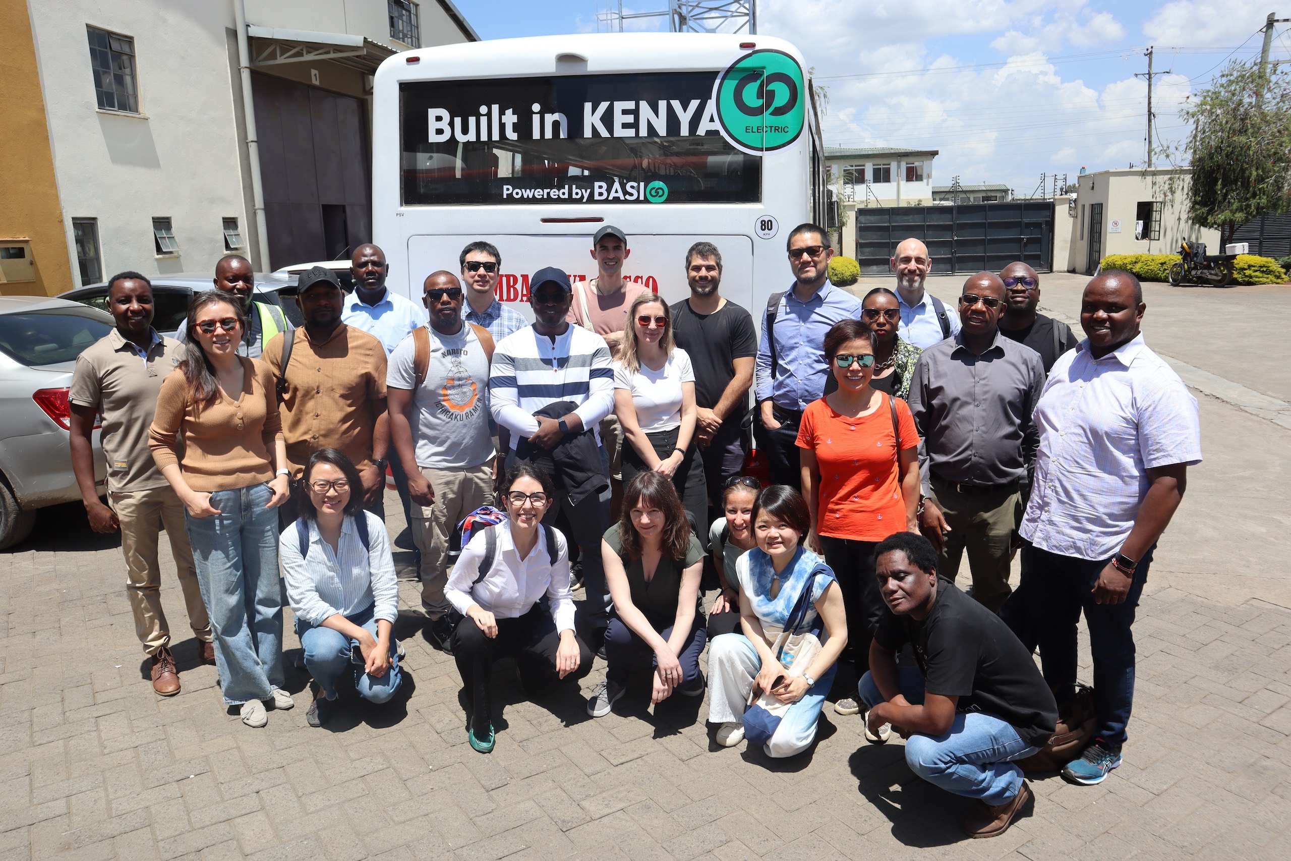 A group of people pose for a photo in front of a electric bus 