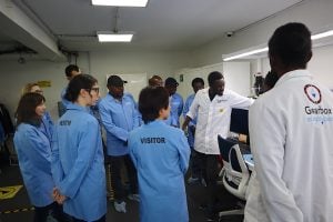 A group of people in lab coats gathered around and looking at some screens