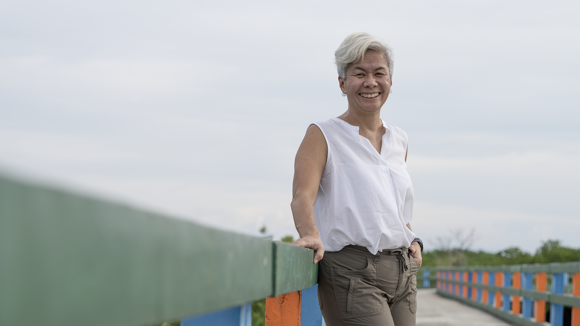 A woman with white hair stands on a bridge