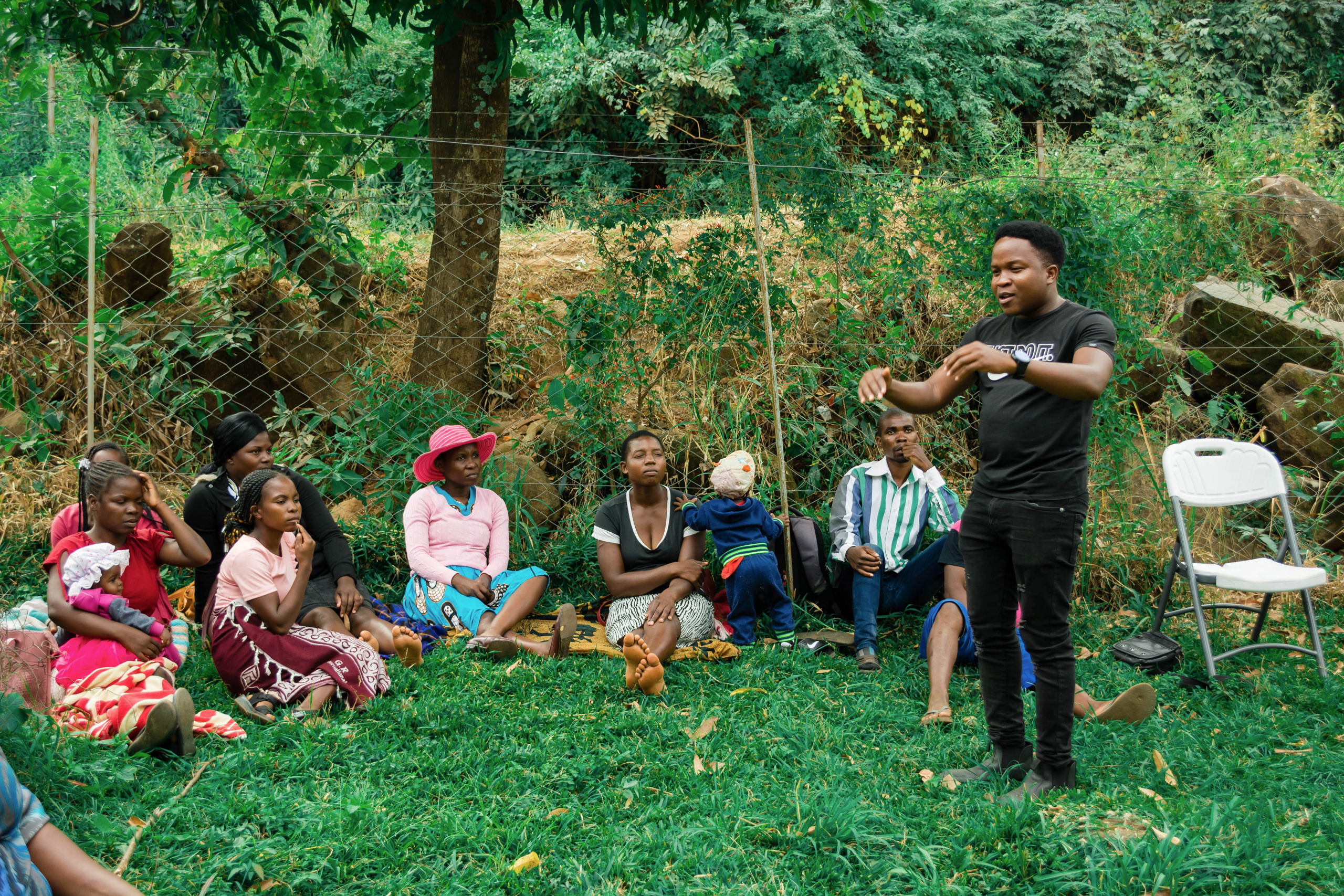 gesturing man standing among people seated on grass