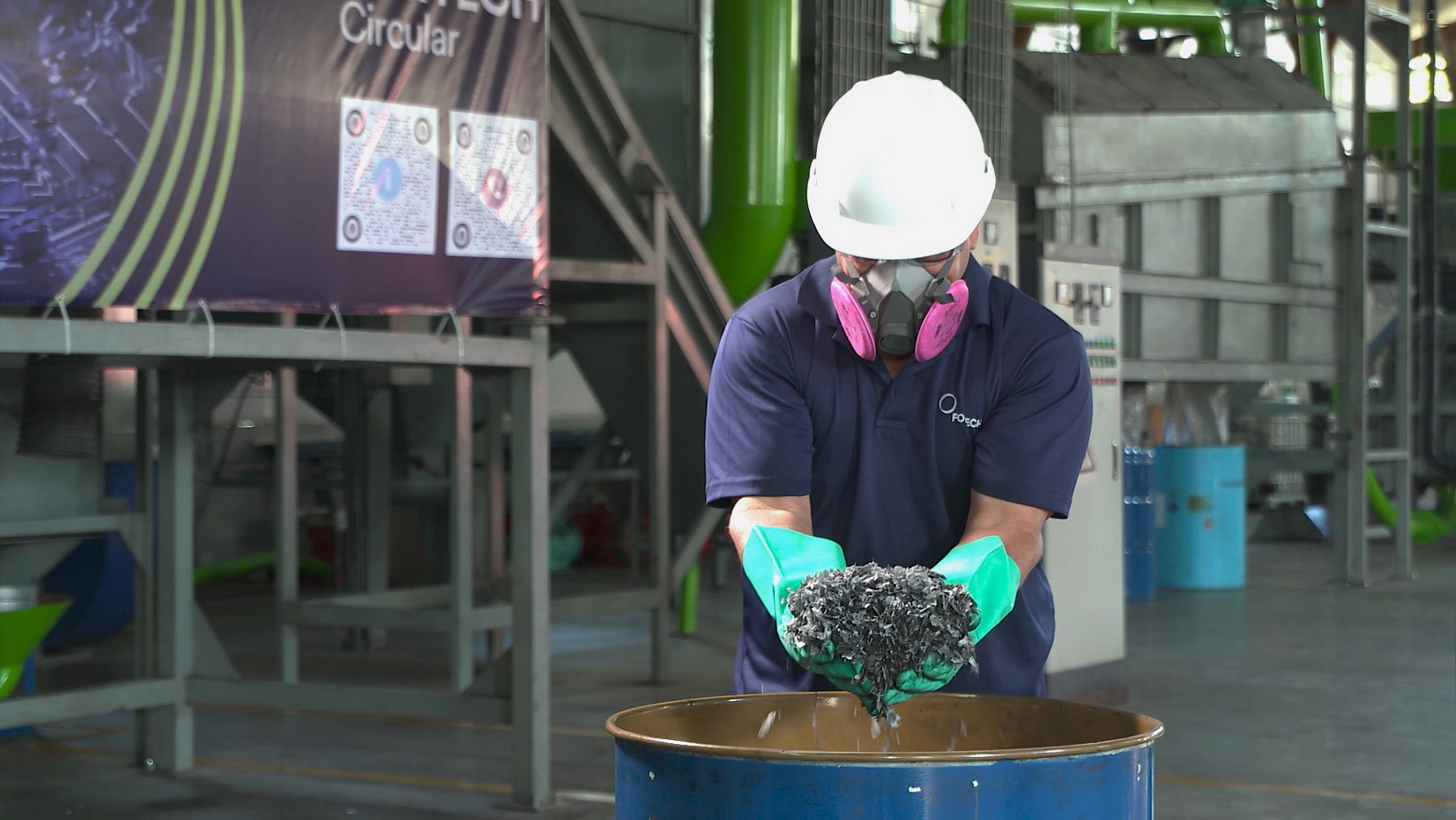 man wearing ppe holding shredded batteries over metal barrel