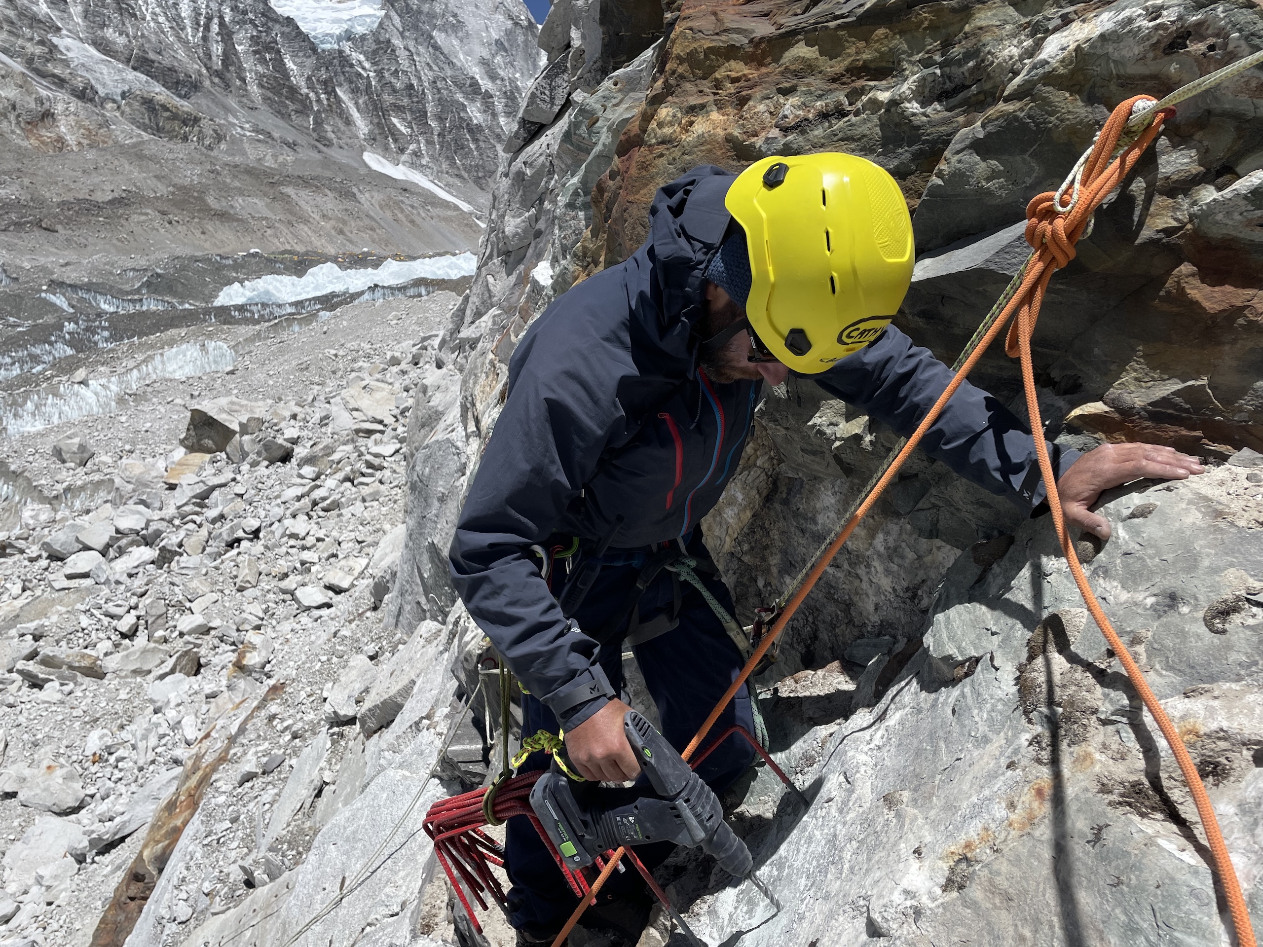 man wearing hard hat on side of rocky mountain drilling hole into rock face