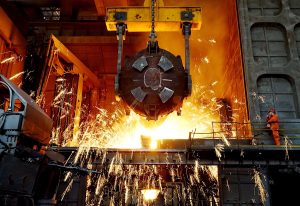 Molten metal pours from a large industrial ladle, emitting bright sparks in a steel factory