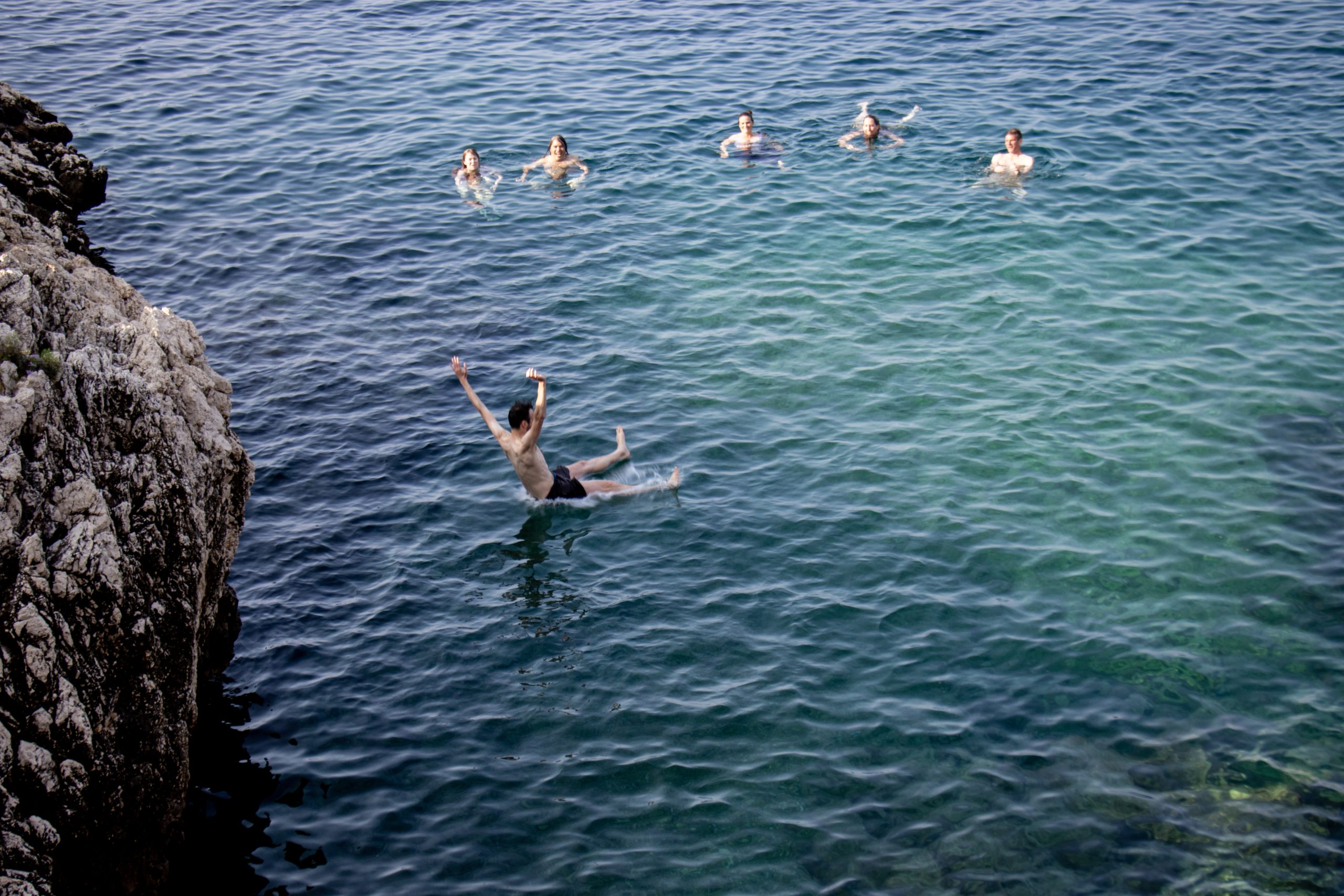 people in water beneath cliff