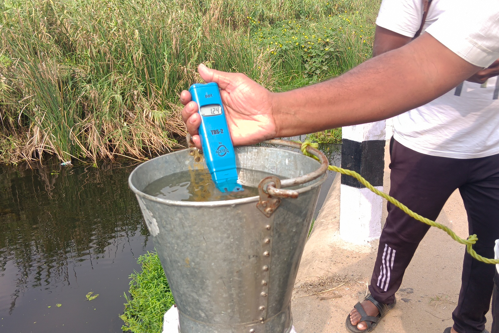 A man holds a tool into a bucket of water to exam the water quality
