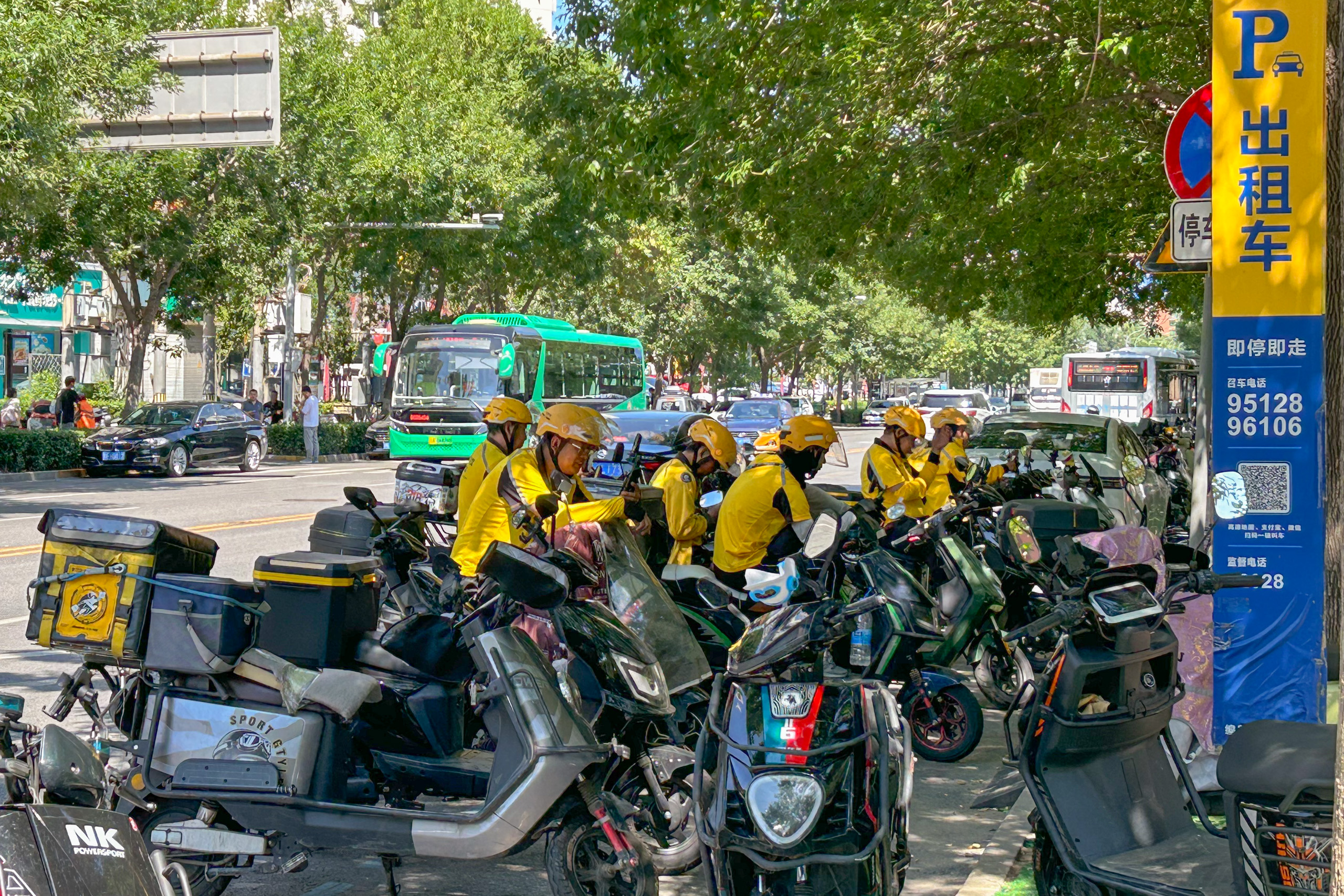 Delivery couriers sit on their mopeds in the shade to escape the heat