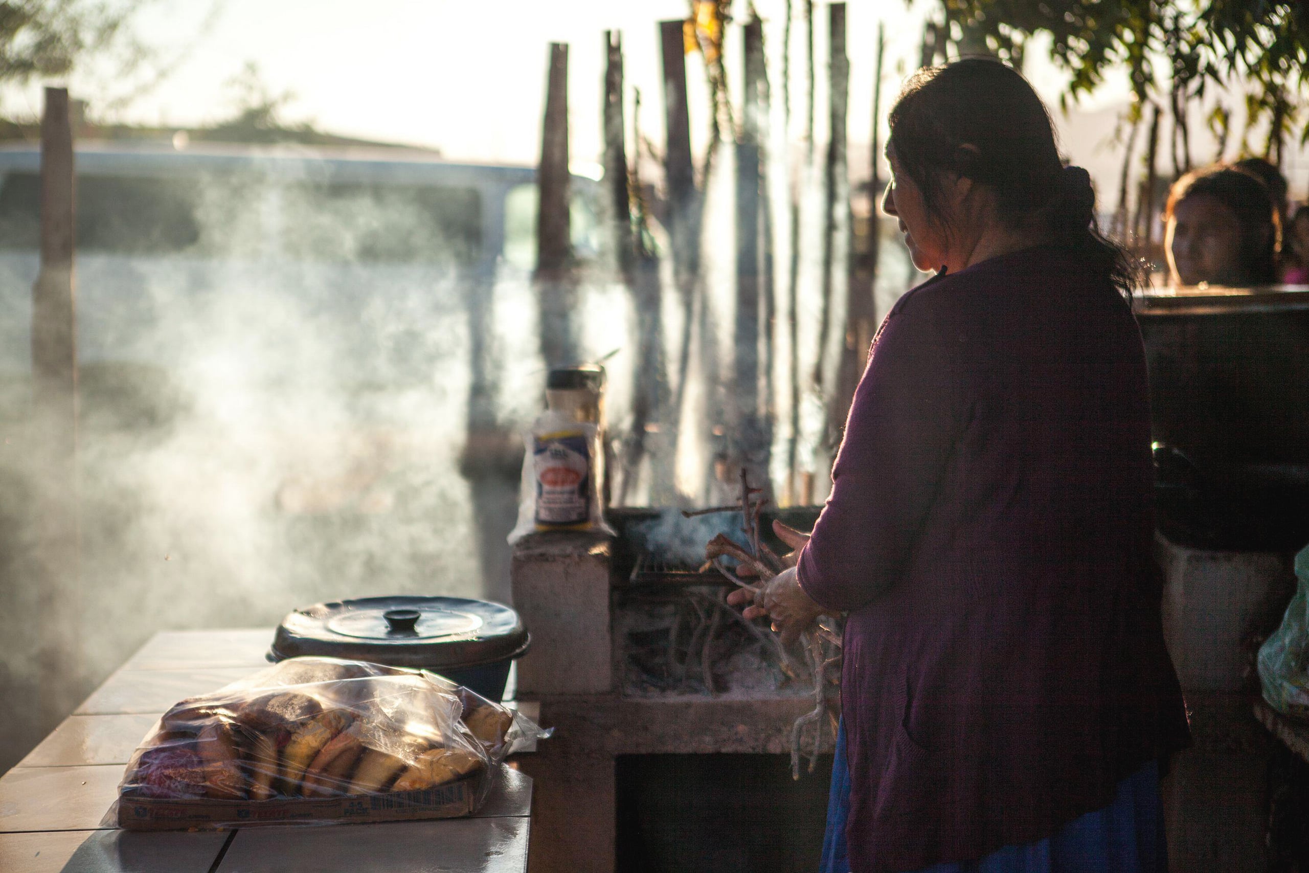 Indigenous woman cooks on a wood stove, smoke