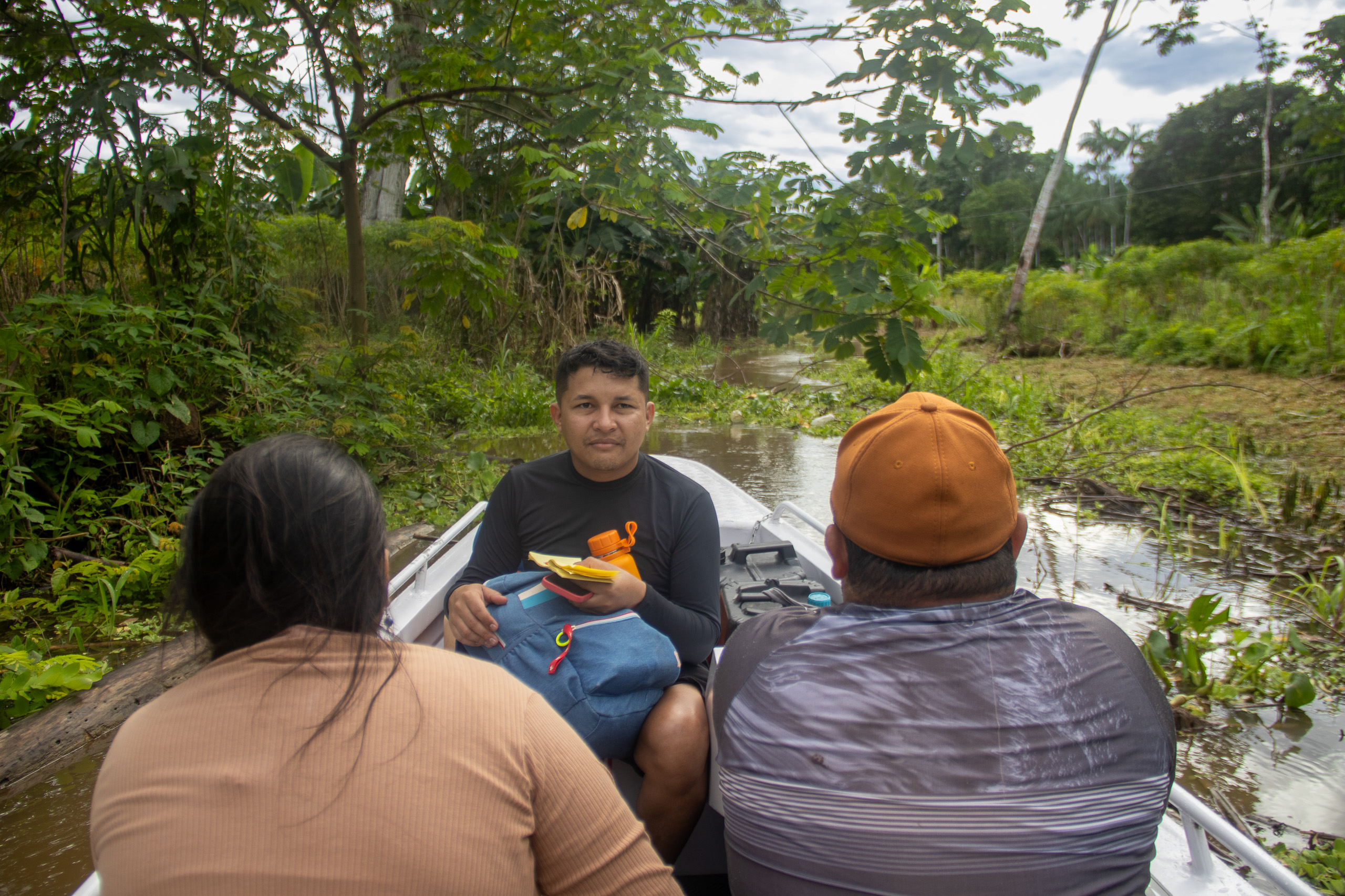 Tres personas en una embarcación estrecha en el agua rodeada de árboles