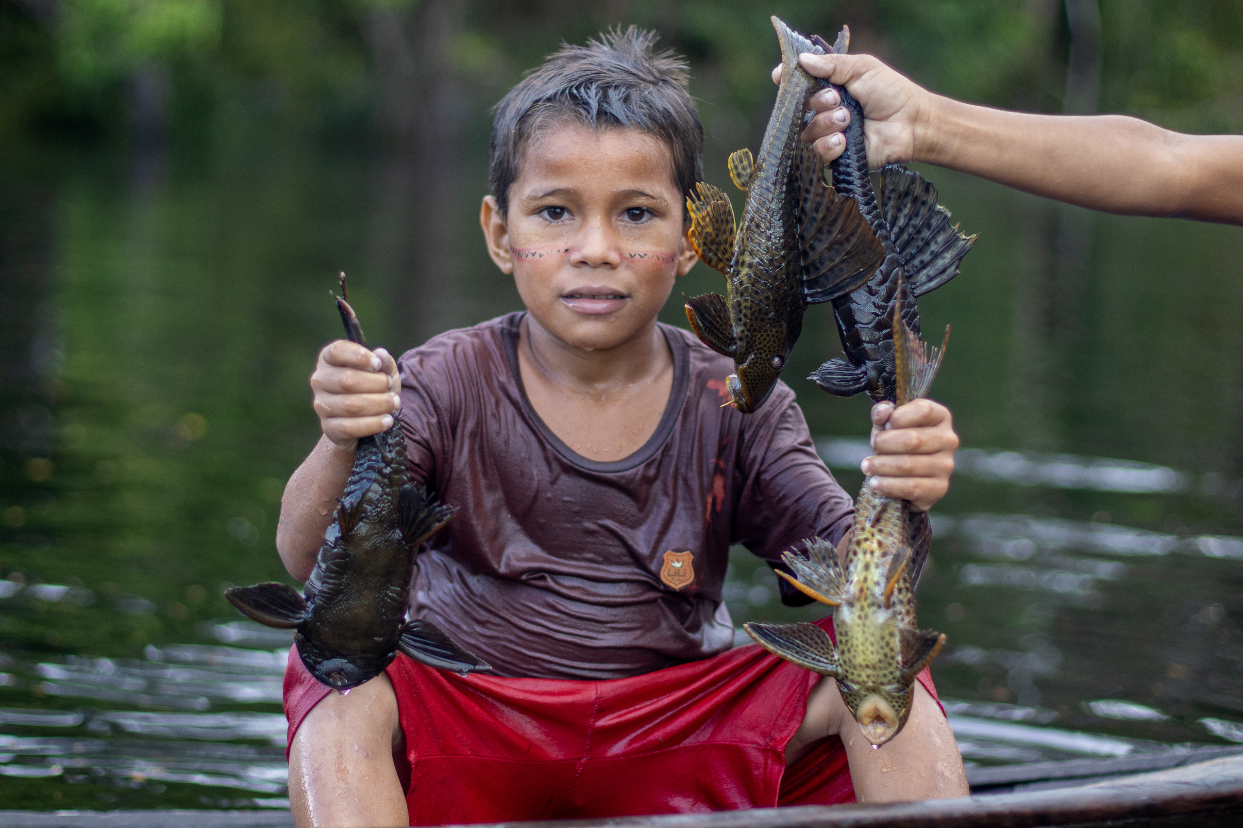 Un niño en una embarcación con pescados en cada mano