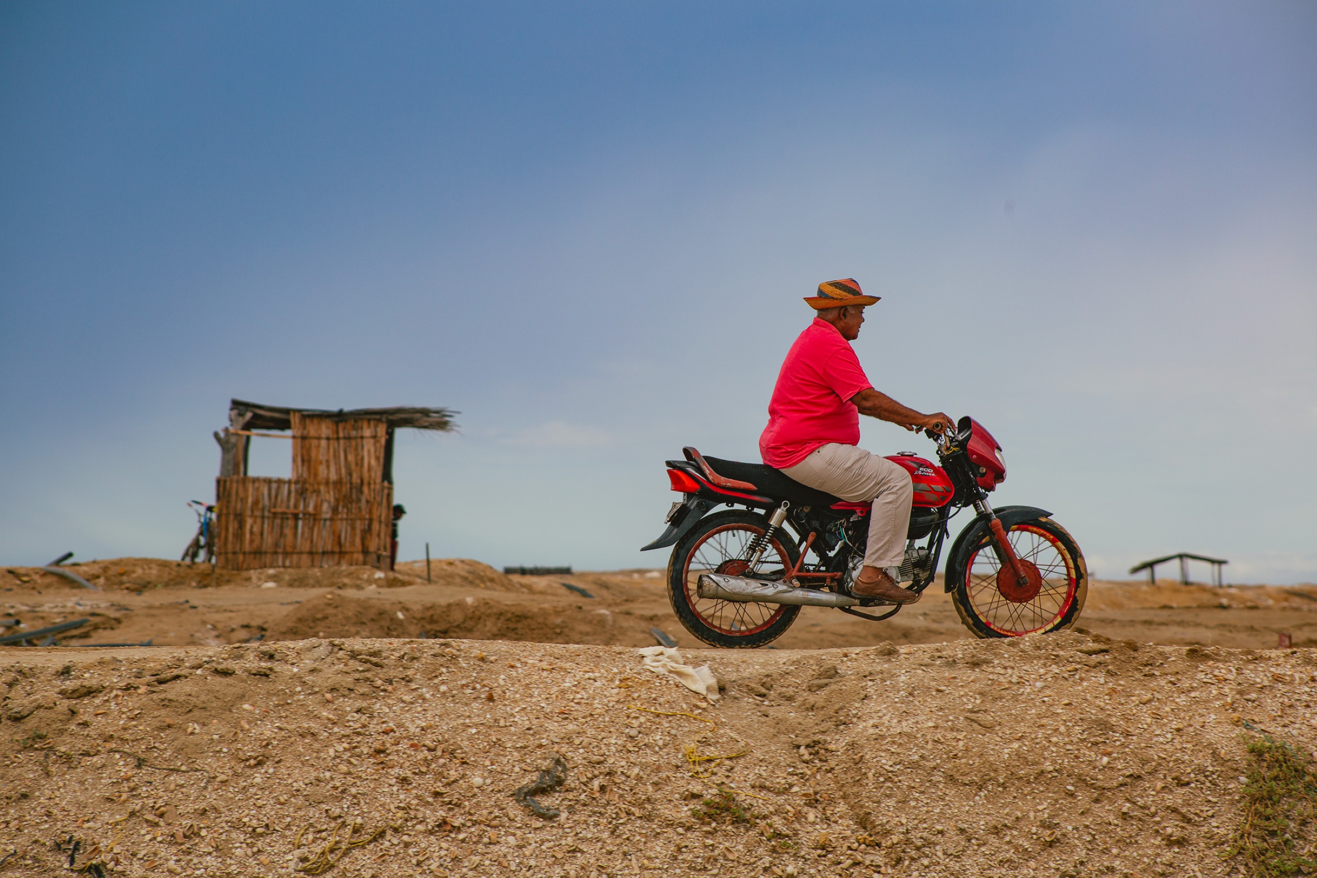 <p>Un hombre conduce una motocicleta en el desierto de La Guajira, en el norte de Colombia. Esta región, una de las más pobres del país, ha sido objeto de proyectos de energía renovable, lo que ha generado tensiones entre las comunidades indígenas locales (Imagen: <a href="https://flic.kr/p/2oKP6sY">Iván Otero</a> / <a href="https://flickr.com/people/197399771@N06">Presidencia de la República de Colombia</a>, <a href="https://creativecommons.org/publicdomain/mark/1.0/deed.pt-br">PDM</a>)</p>