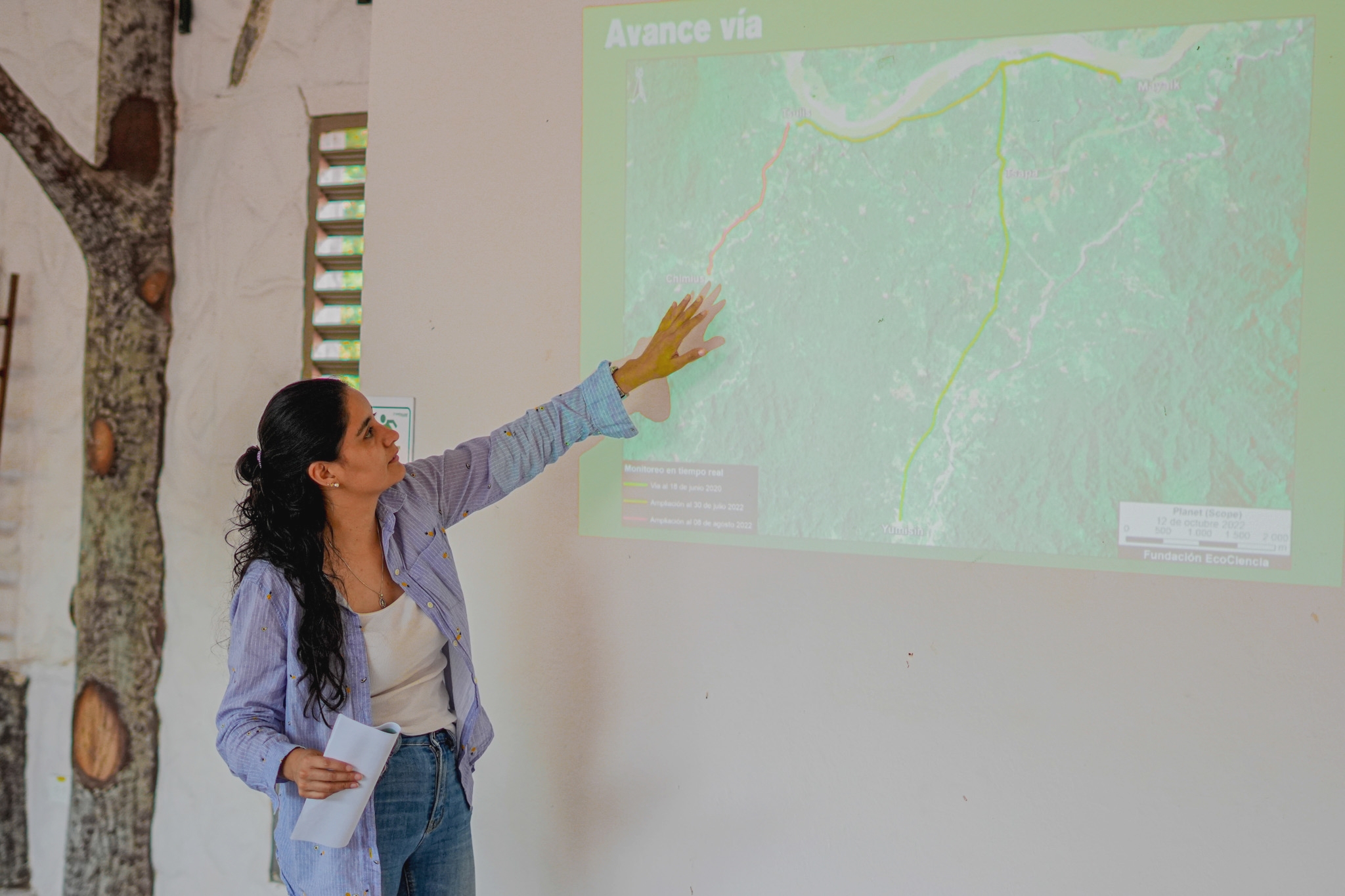 mulher e camisa social e calças jeans mostra mapa na parede branca com projetor