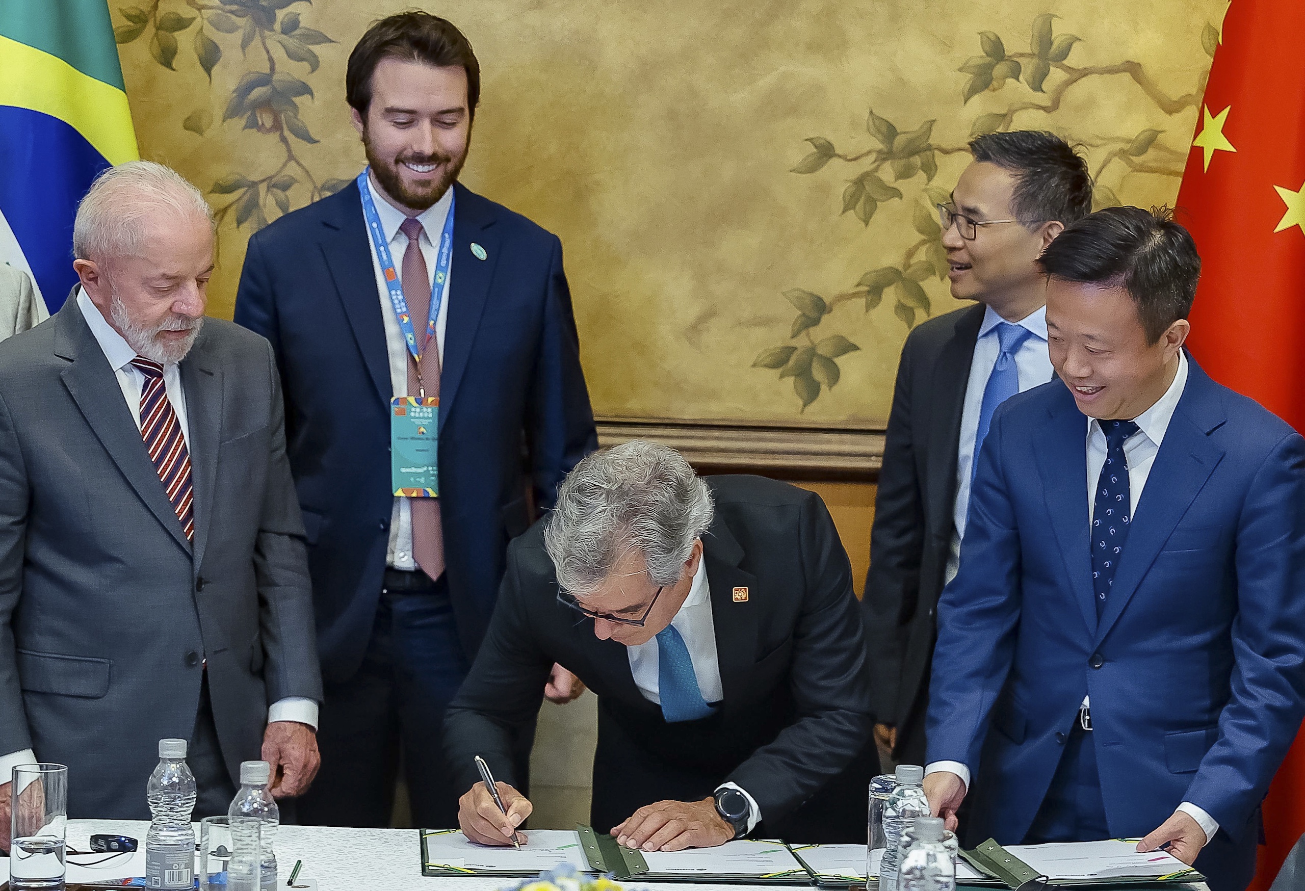 Lula da Silva junto a outros quatro homens vestidos de terno, enquanto um deles assina um documento