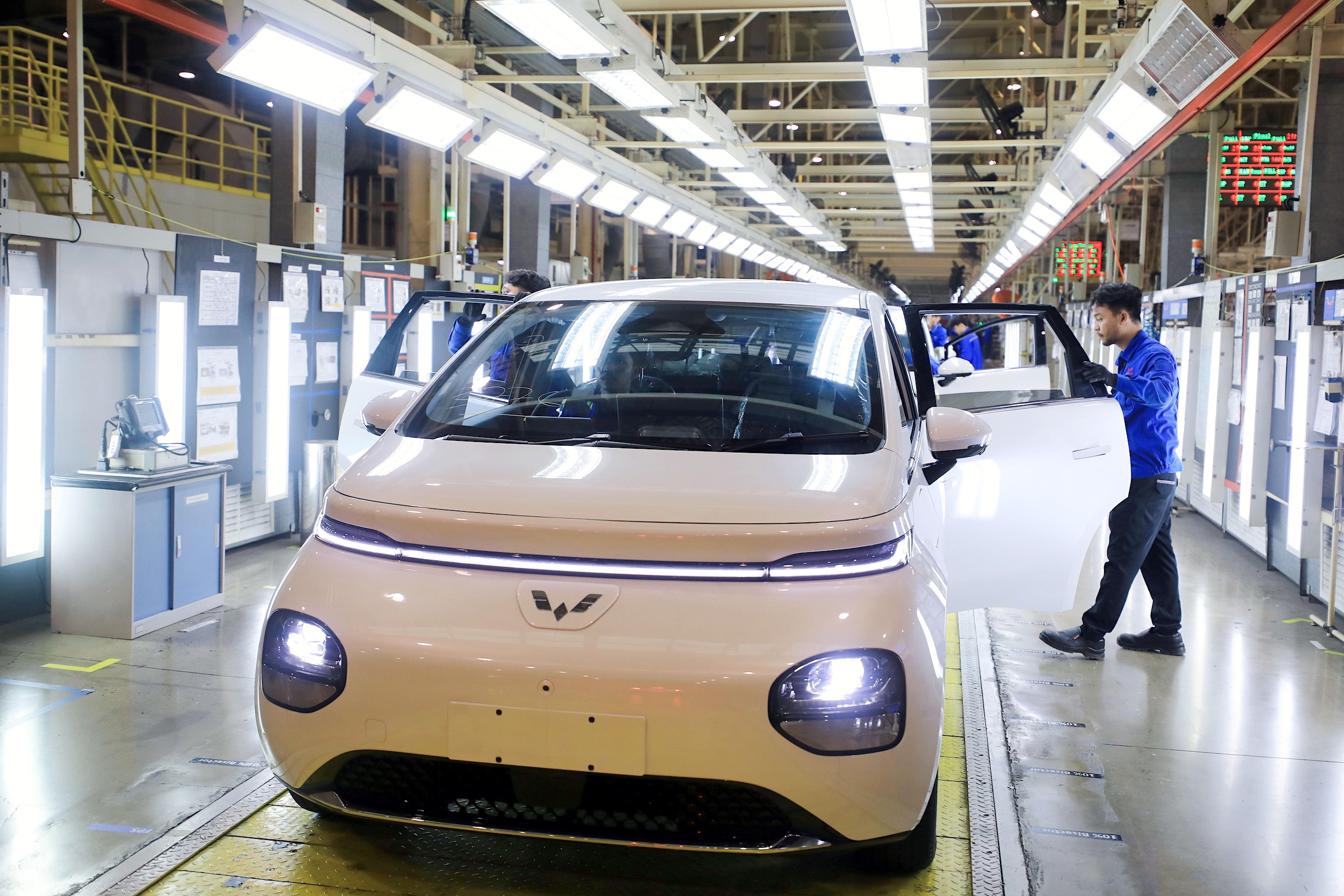 A man stands beside a car on an assembly line