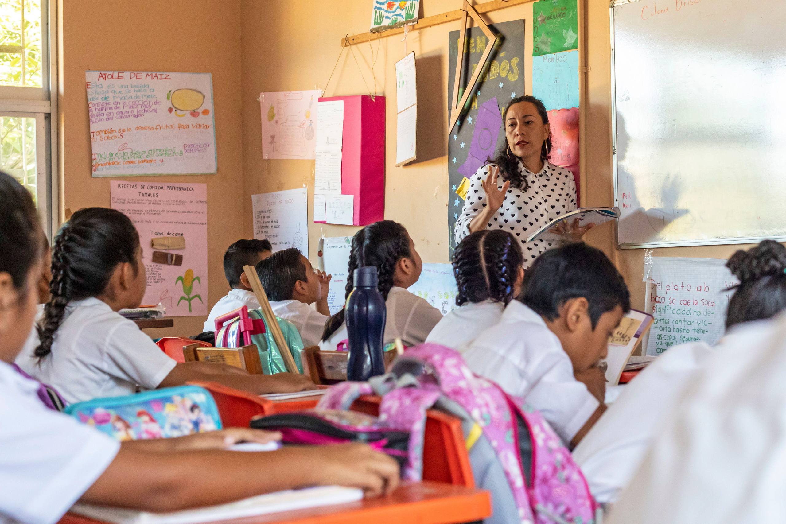 Niños en un aula escuchando a su maestra