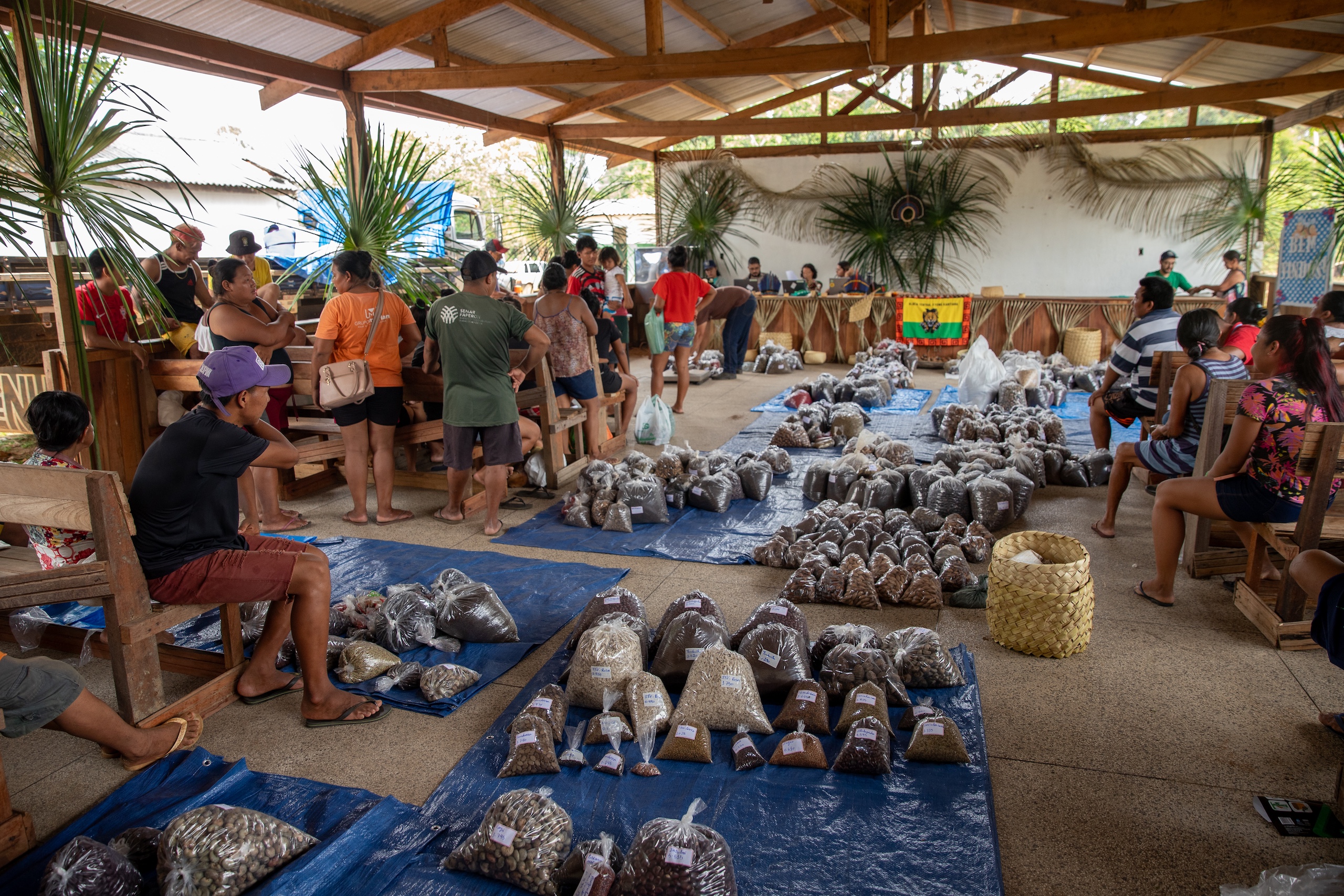People sitting in a hall, among bags of goods laid out on blue tarps