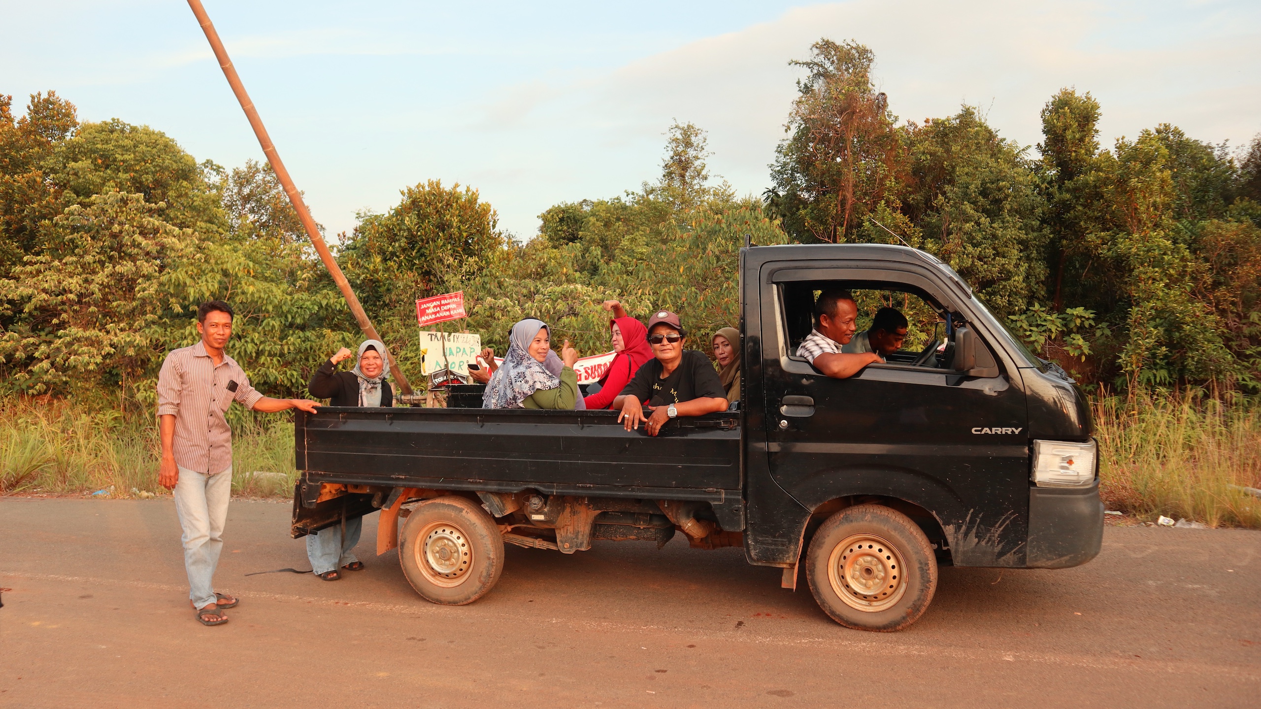 Several passengers holding protest signs seating on the back of a small black truck parked on a roadside
