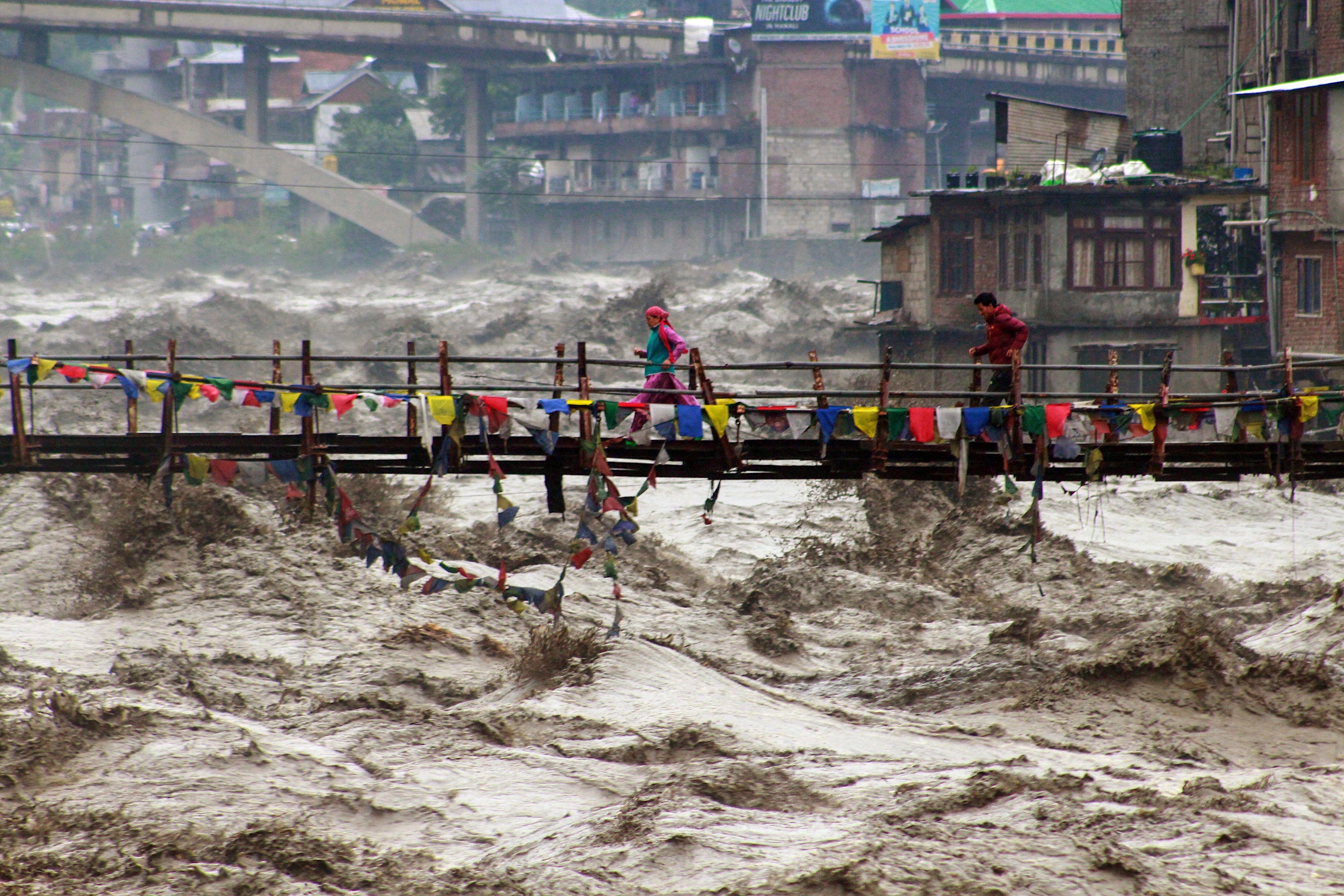<p>People run across a bridge over the flooding Beas River in the town of Kullu, Himachal Pradesh following heavy rains on 26 August (Image: Aqil Khan / Associated Press / Alamy)</p>