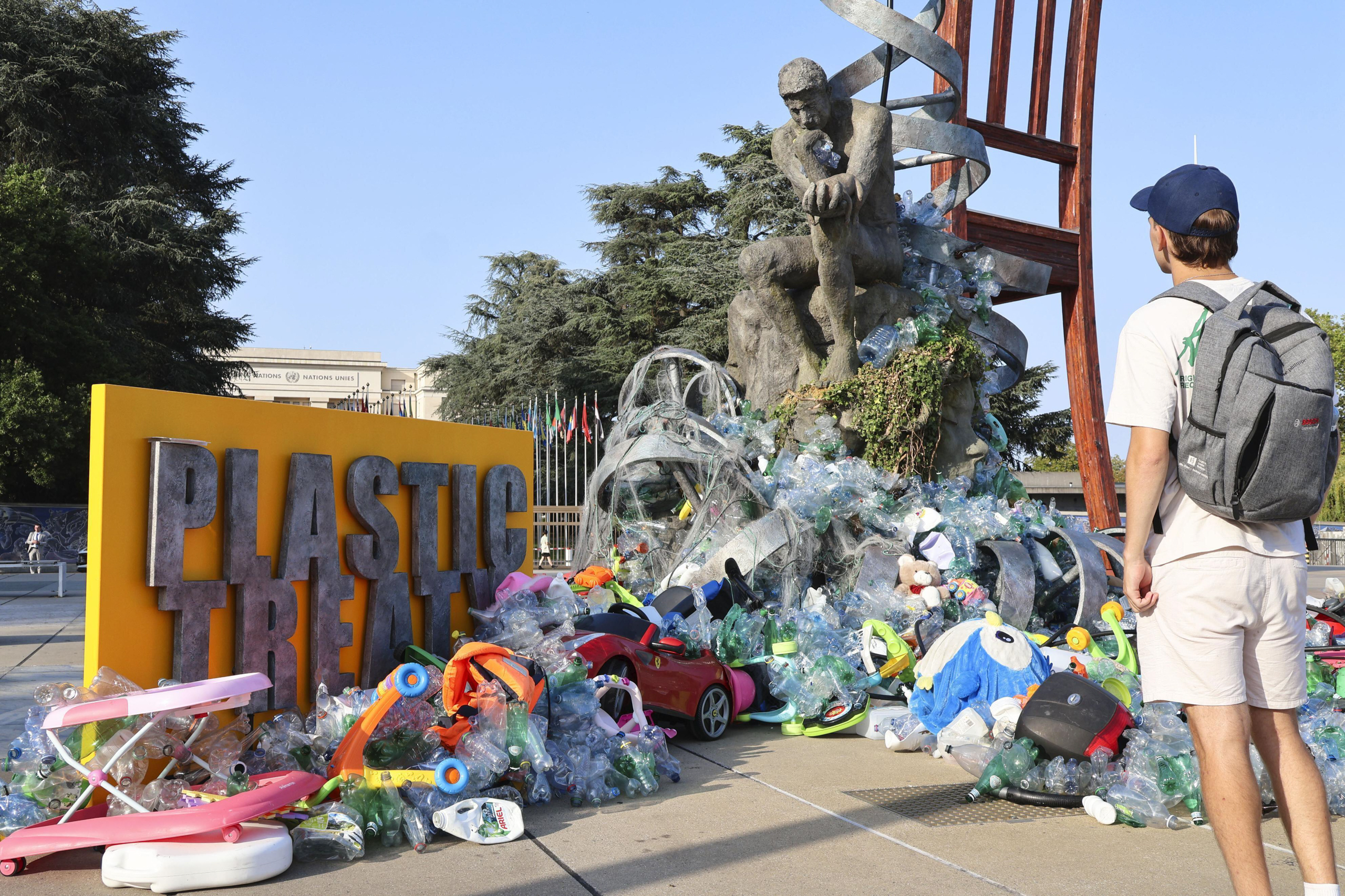 man looking at sculpture of man sitting atop mound of plastic
