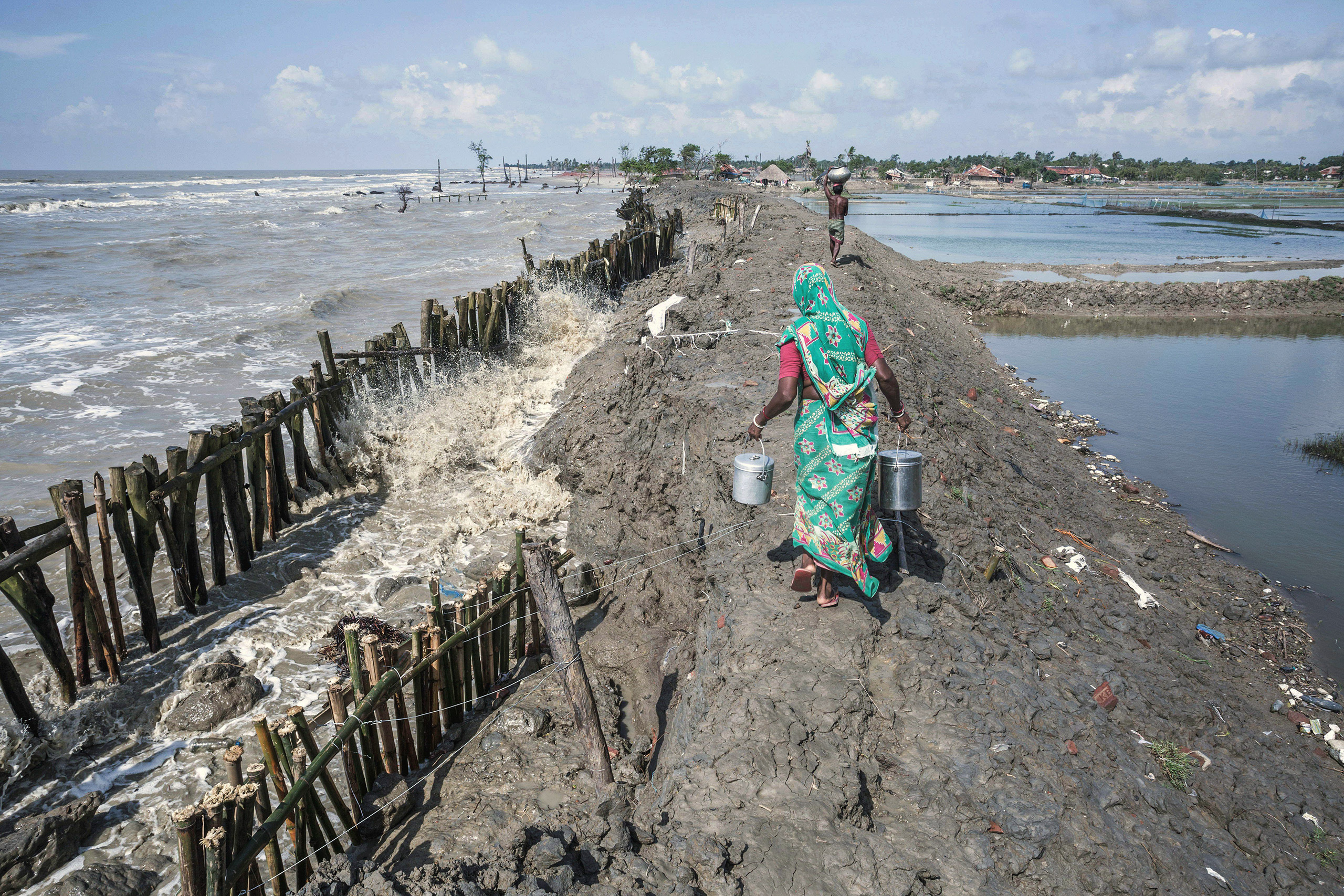 woman holding metal pails walking along muddy embankment 