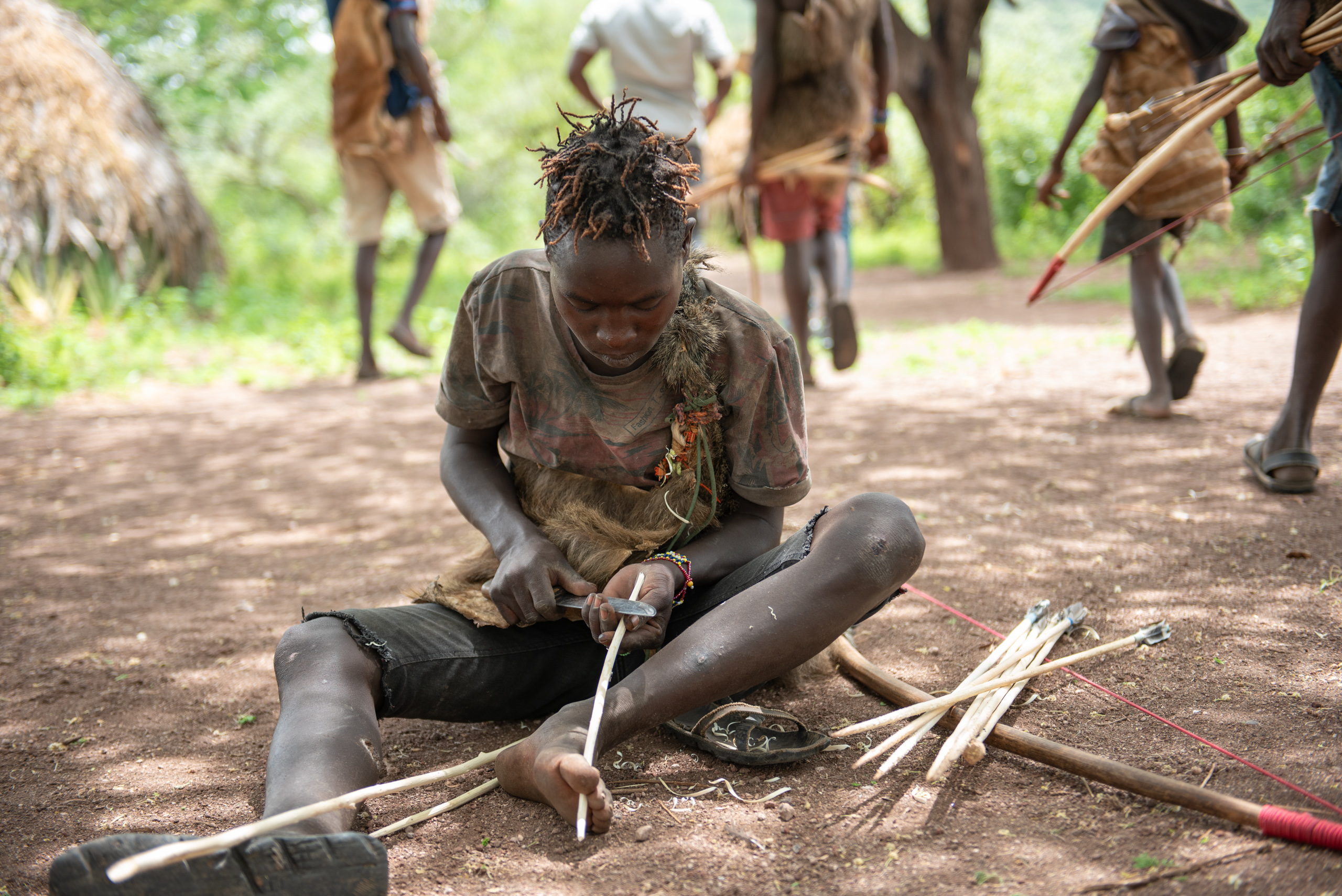 A young man sits on the ground, focused on crafting an arrow