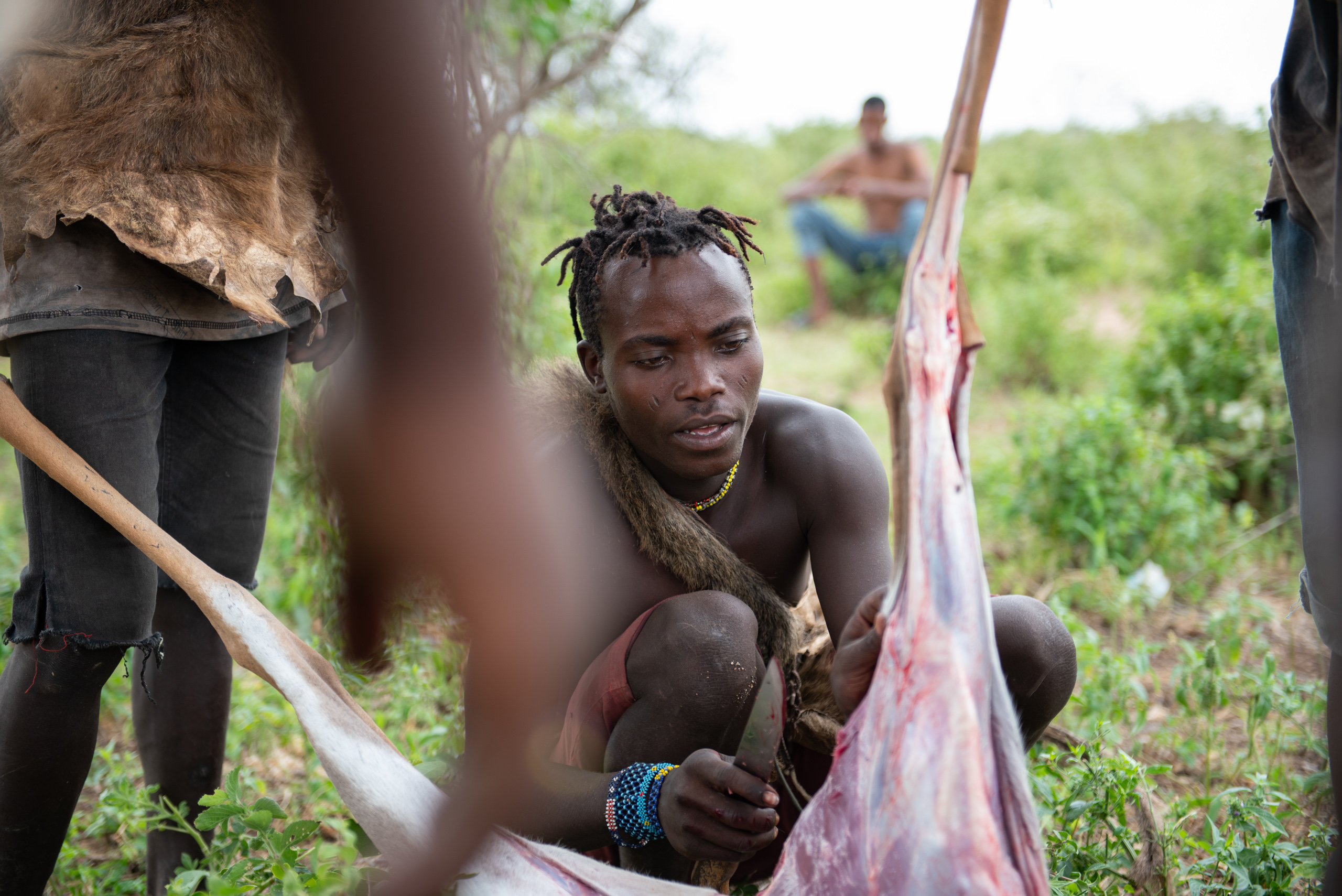 A man wearing traditional clothing, focused on preparing a large piece of meat outdoors
