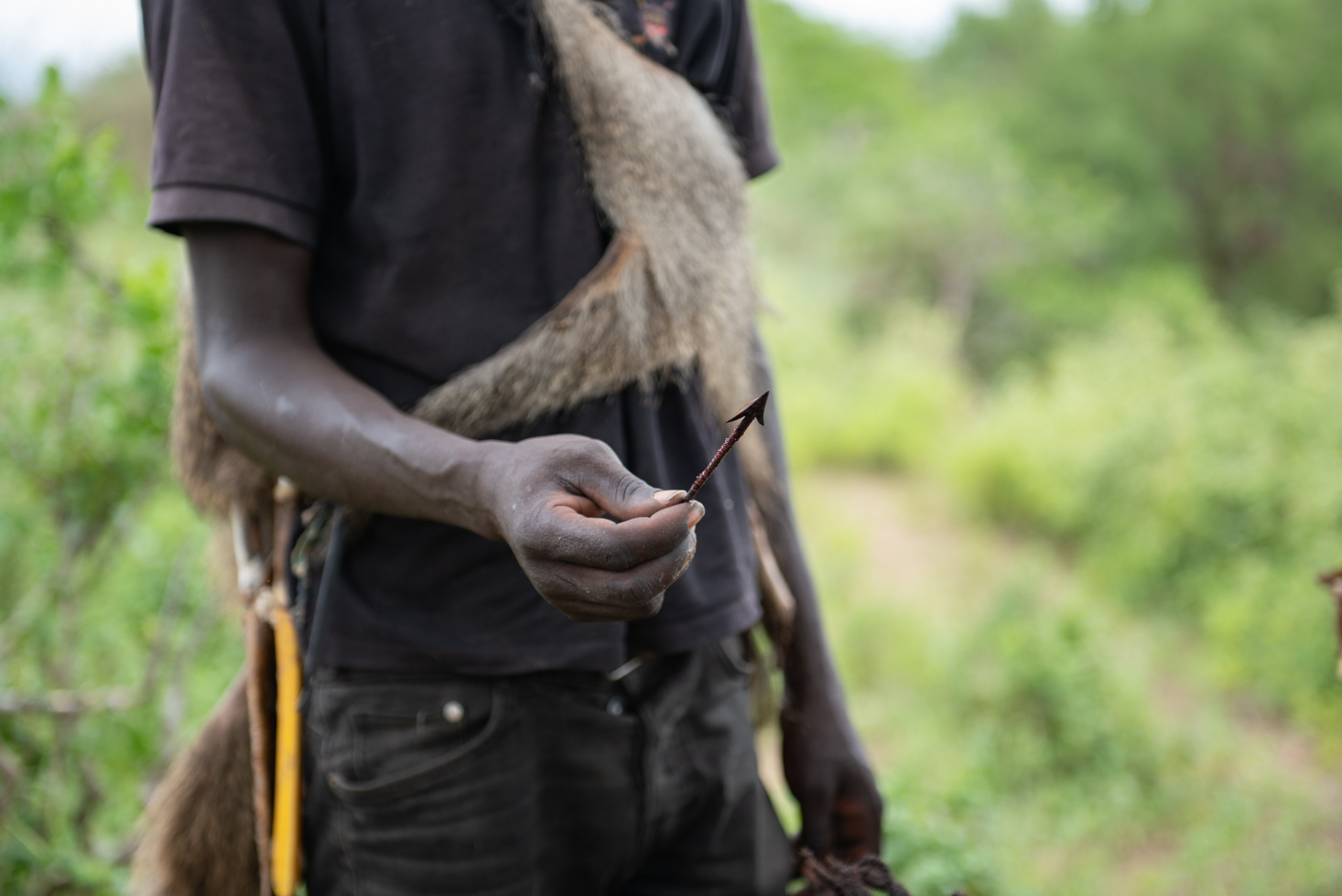 A person in rugged attire holds a small, sharp arrowhead