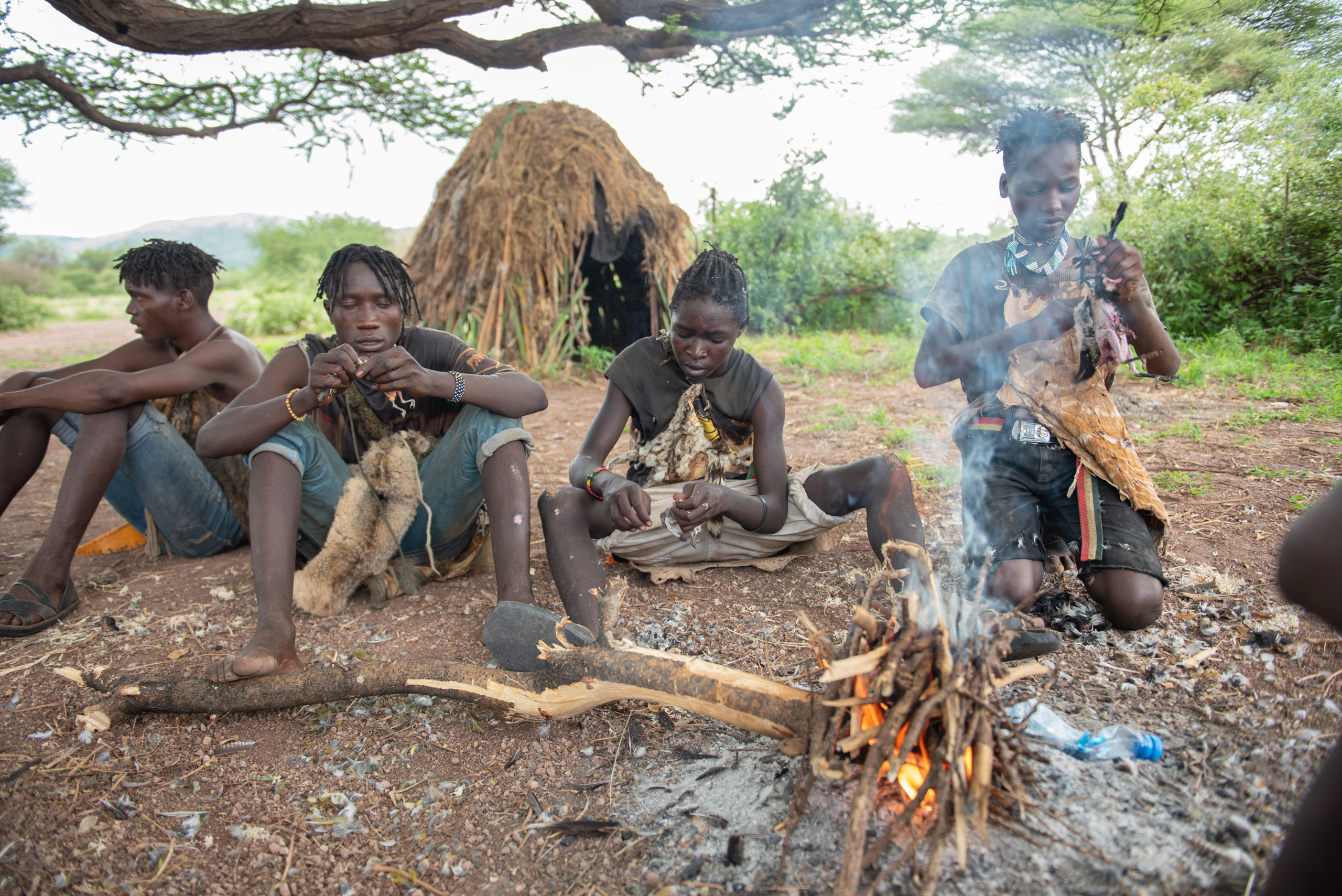 People sit around a small campfire near a thatched hut