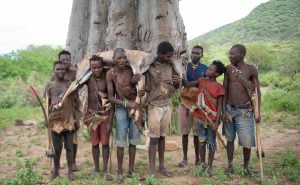 <p>In the remote savannah of northern Tanzania, a group of Hadzabe hunters pose in front of a baobab tree after a successful kill (Image: David Mkazi / Dialogue Earth)</p>