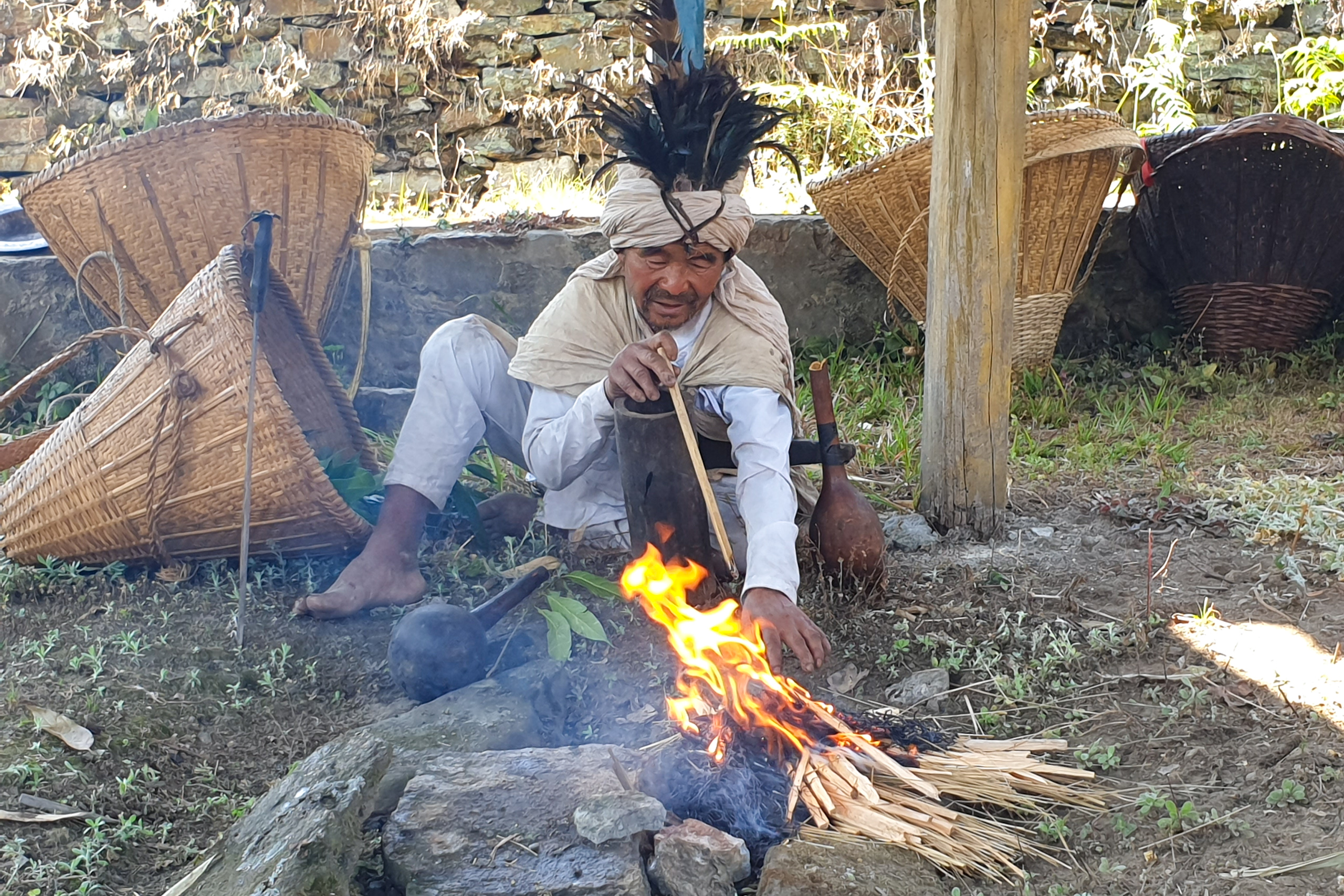 Man in ceremonial clothing stokes small fire