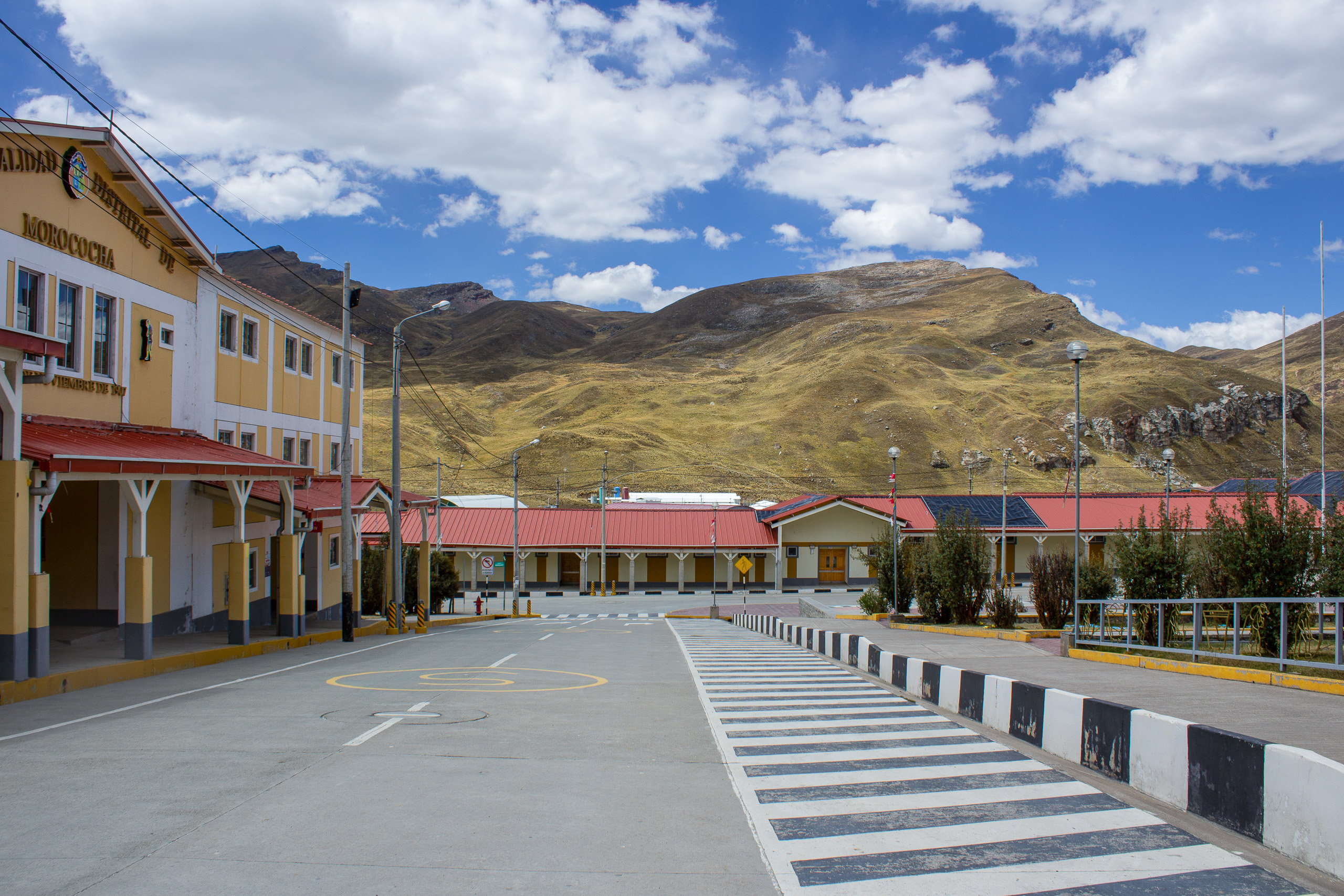 A paved street with a zebra crossing leads to yellow buildings with red roofs
