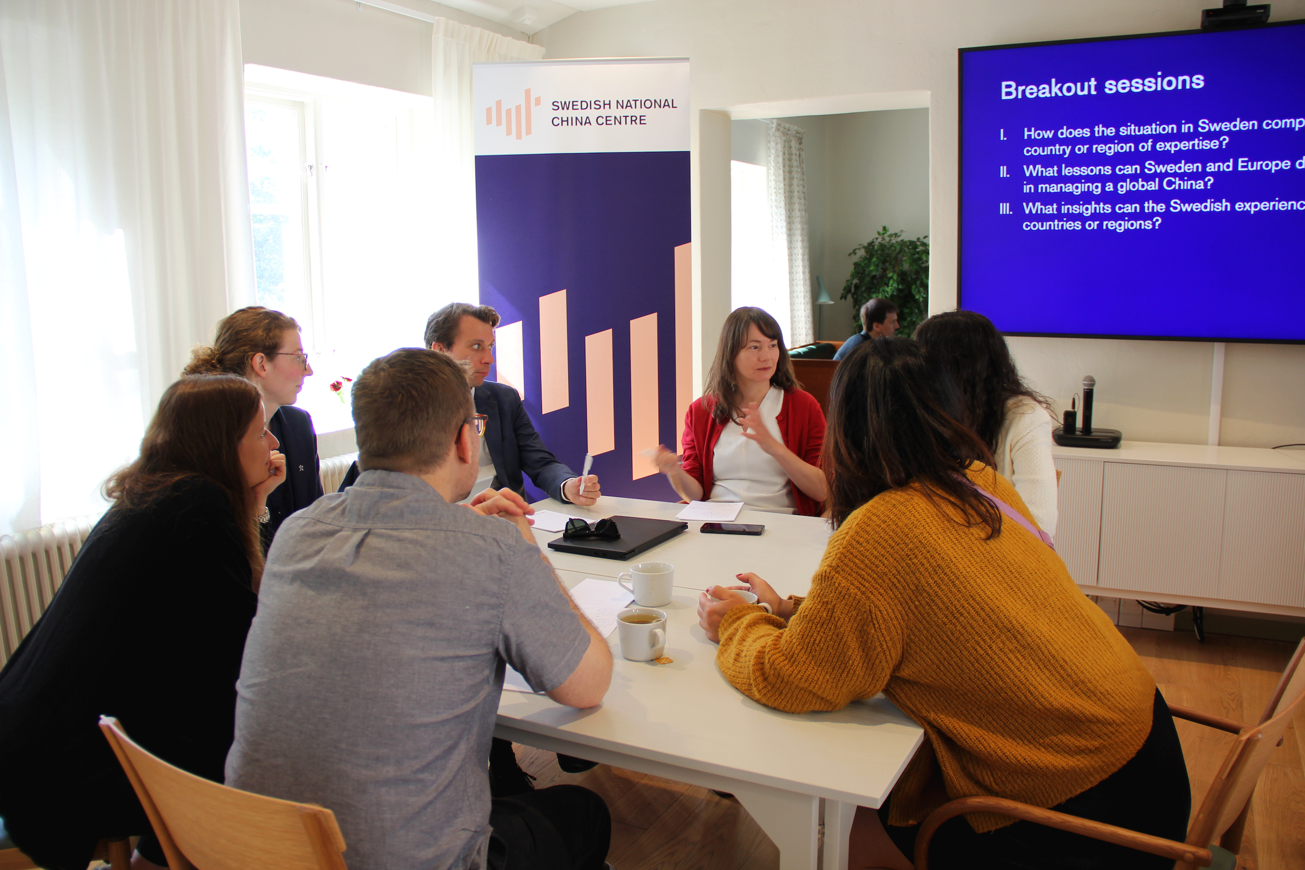 A group of people engaged in a discussion at a table, with a presentation screen behind