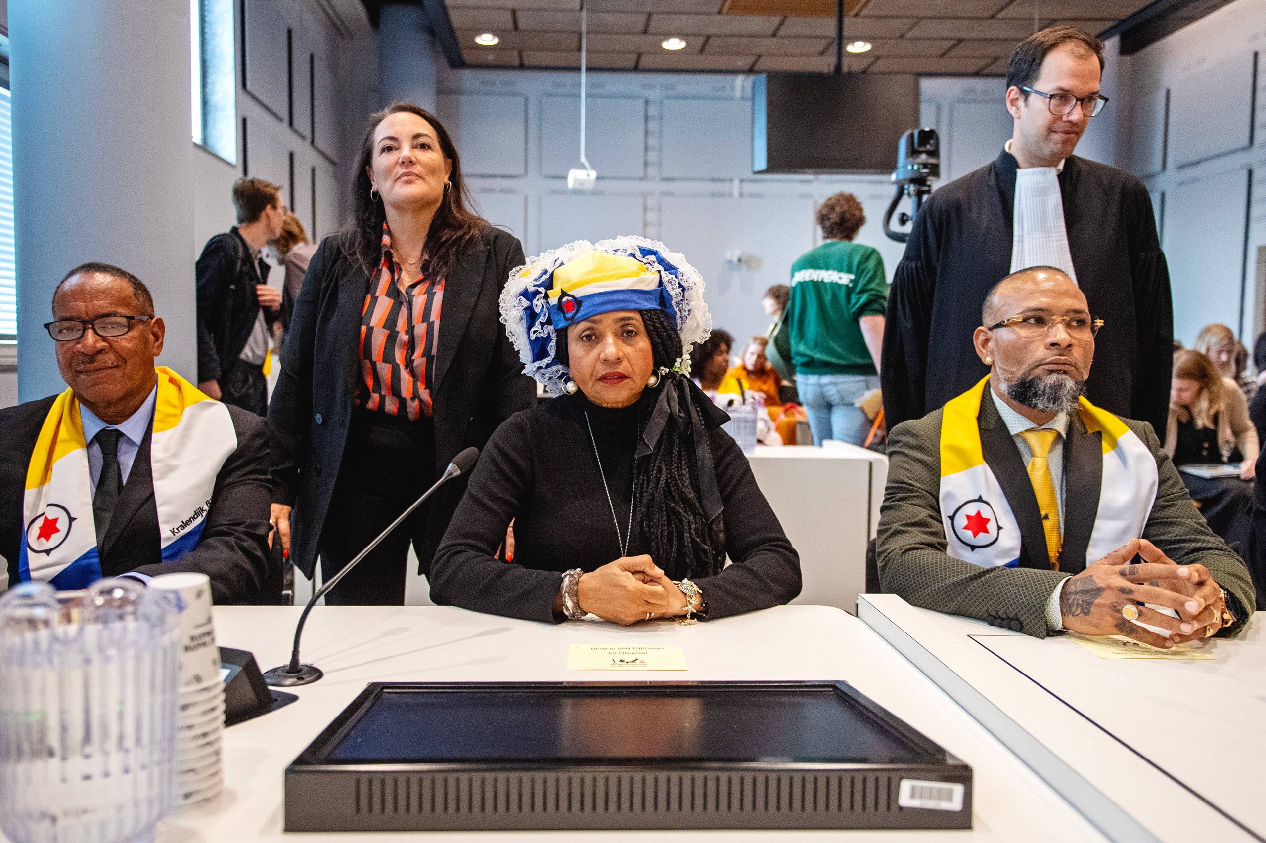 Un grupo de personas sentadas durante un evento formal, vestidas con atuendos distintivos