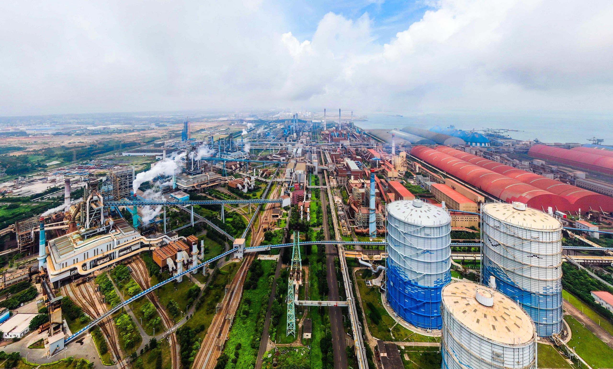 Aerial view of an industrial complex with smokestacks, large storage tanks, and rail lines 