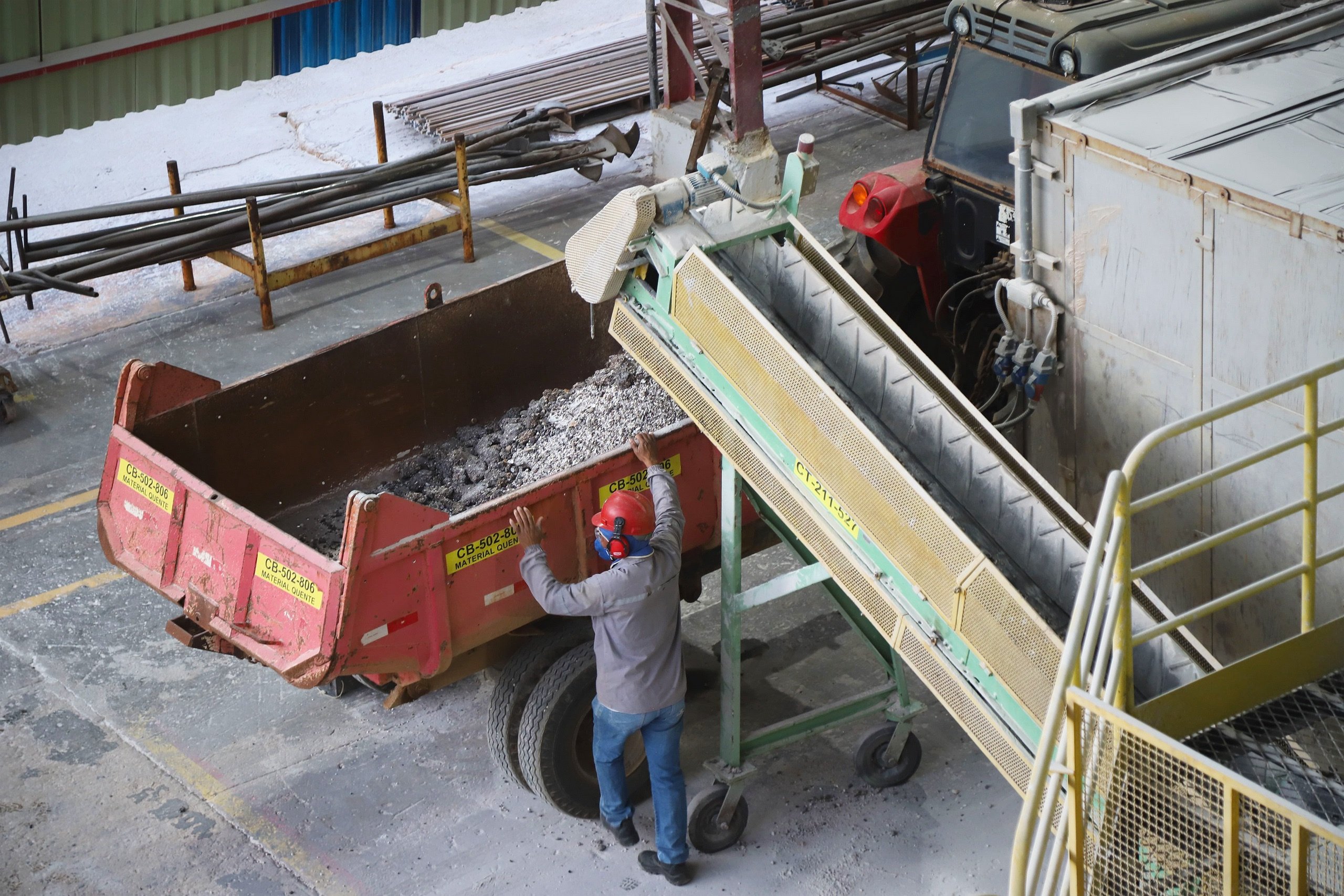 Un trabajador con casco rojo carga material de una cinta transportadora a un camión