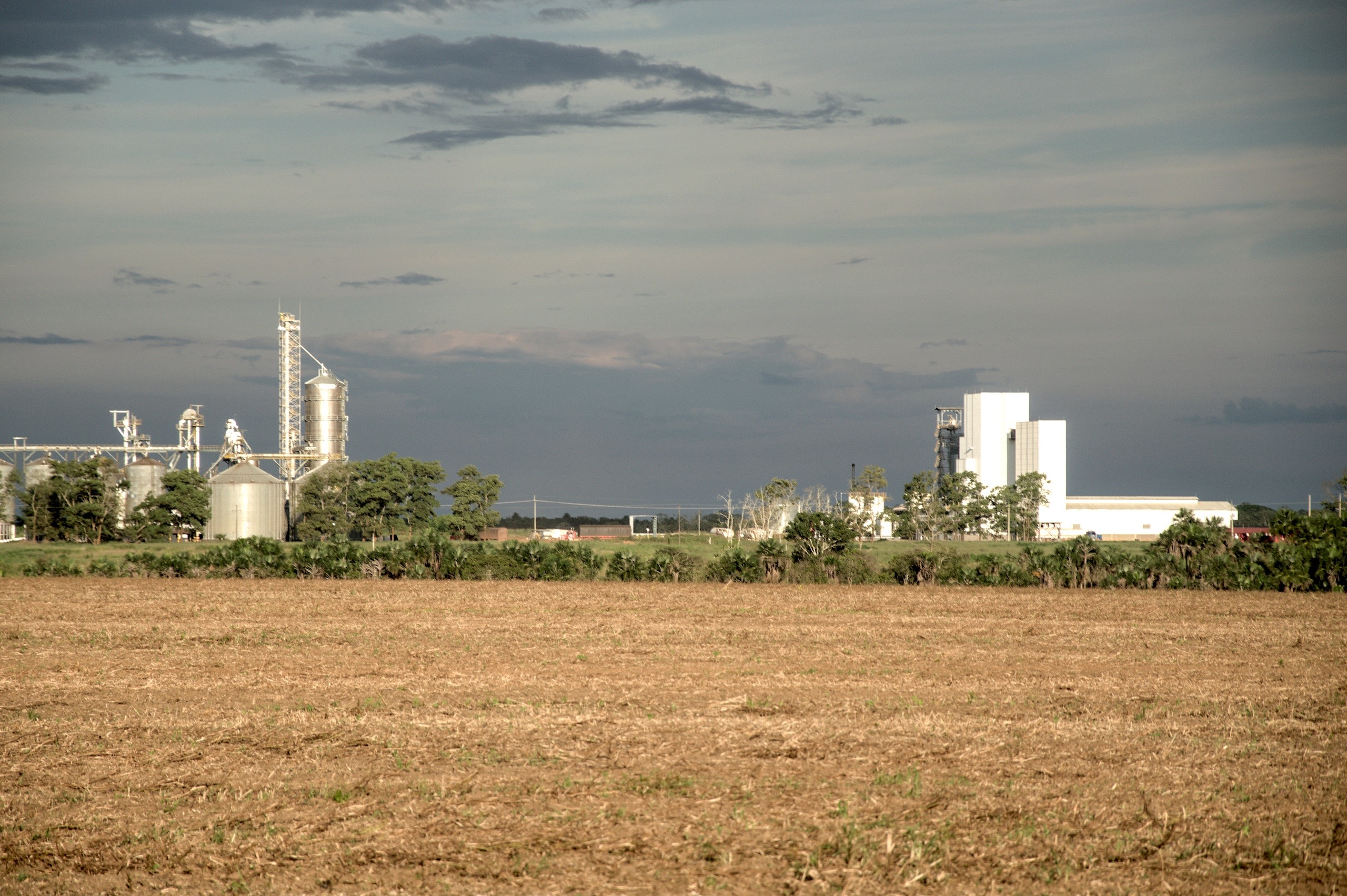 A wide view of an agricultural landscape  and industrial buildings in the far end