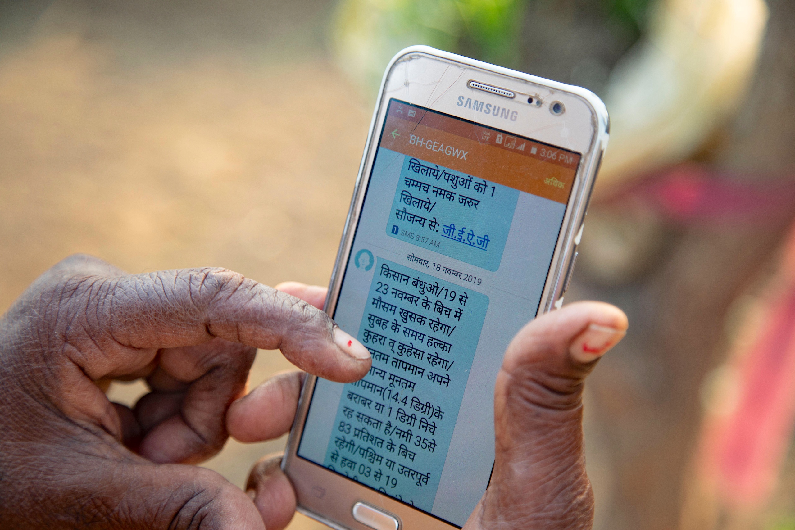 A person holds a smartphone displaying a Hindi text message related to weather updates