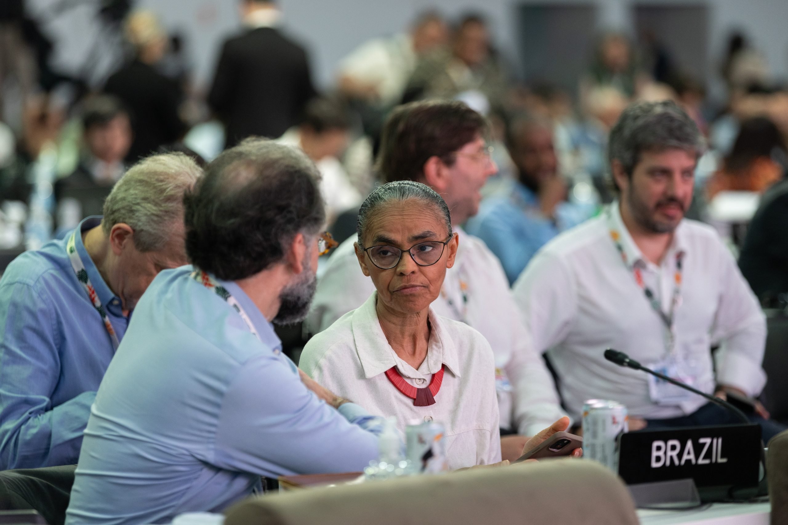 Marina Silva sentada frente a una mesa con un micrófono y un cartel que dice "Brasil"