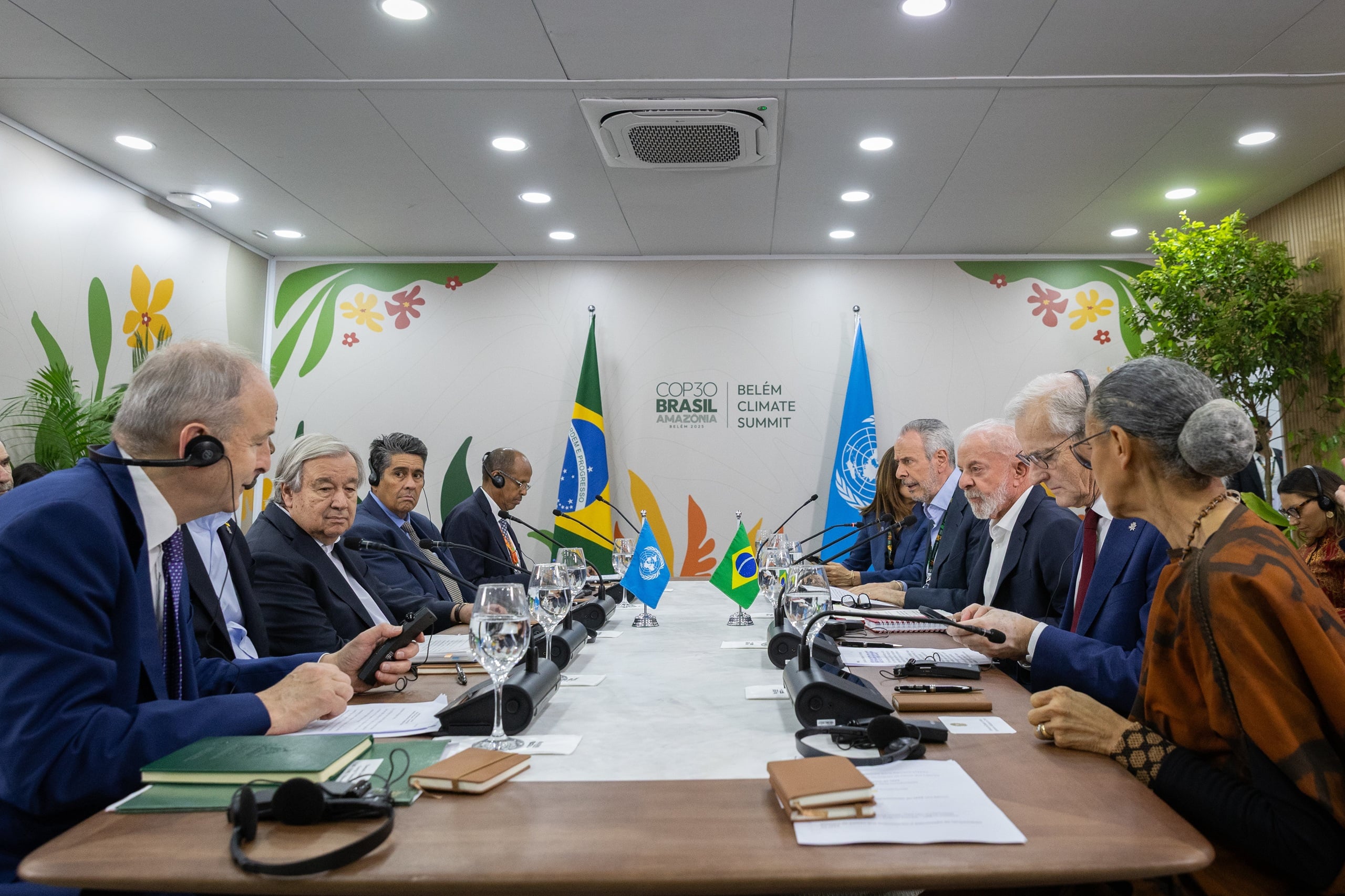Personas sentadas alrededor de una mesa larga, con banderas de Brasil y la ONU en el fondo
