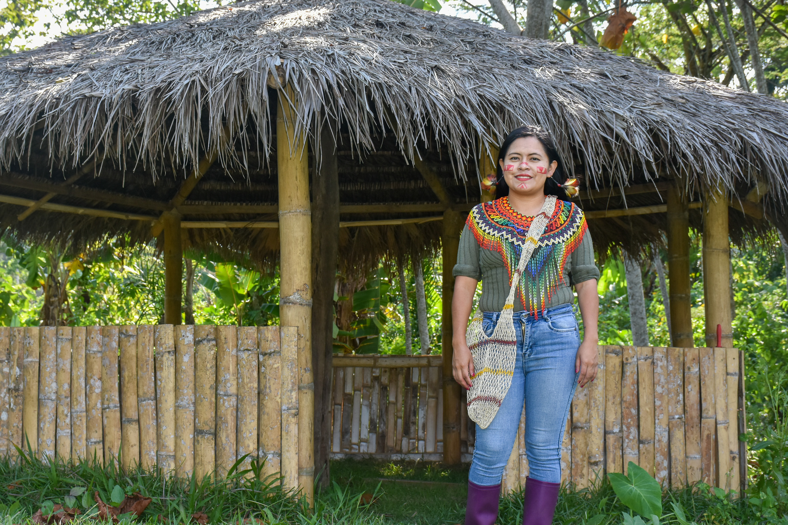 A woman in traditional native dress stands in front of a thatched hut