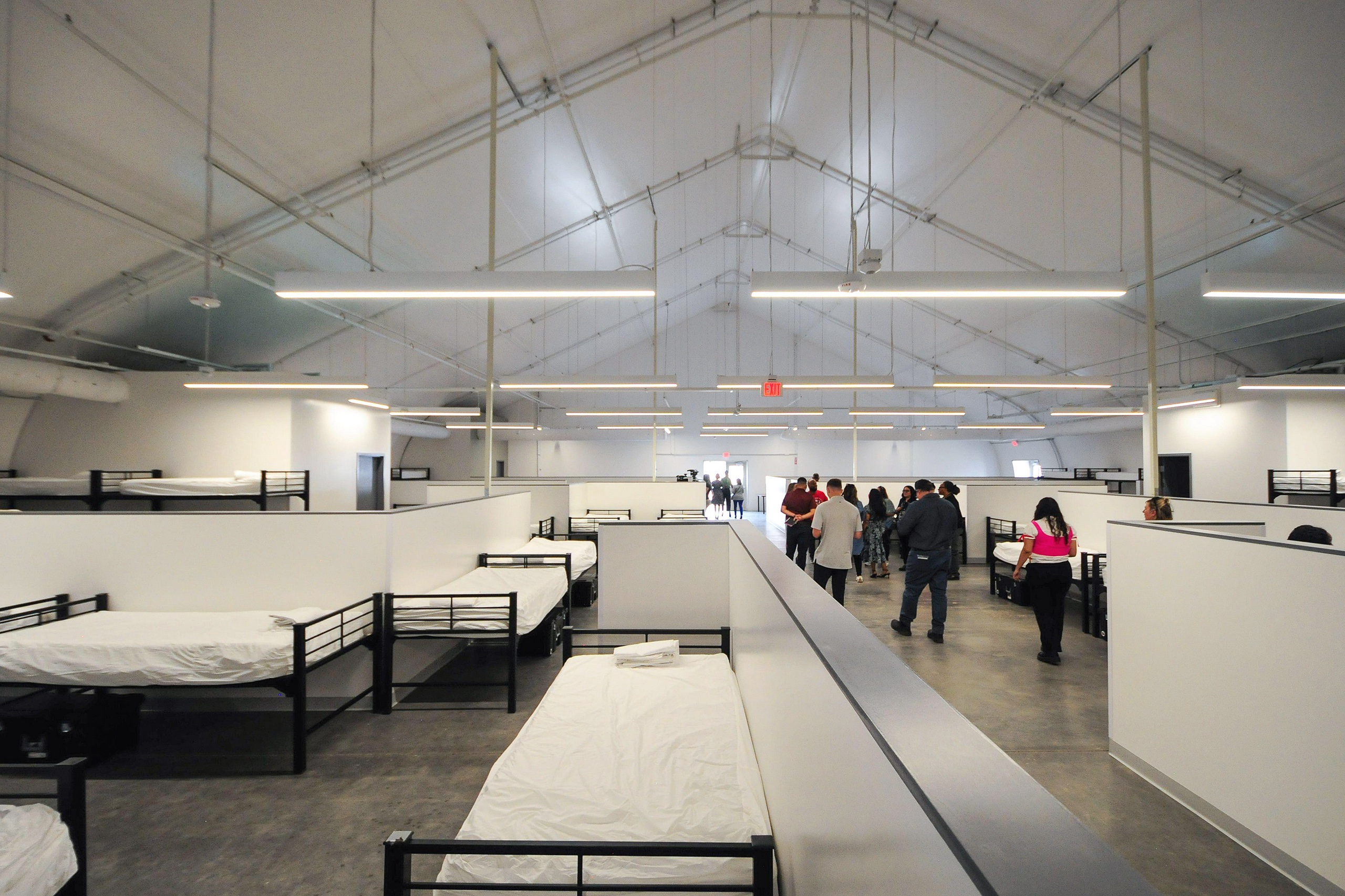 a large, modern shelter with rows of beds and groups of people walking through the space