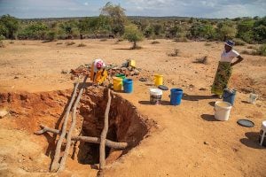 Two women fetch water from a well in a dirt field