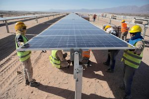 Workers in safety gear install solar panels in a sandy desert environment